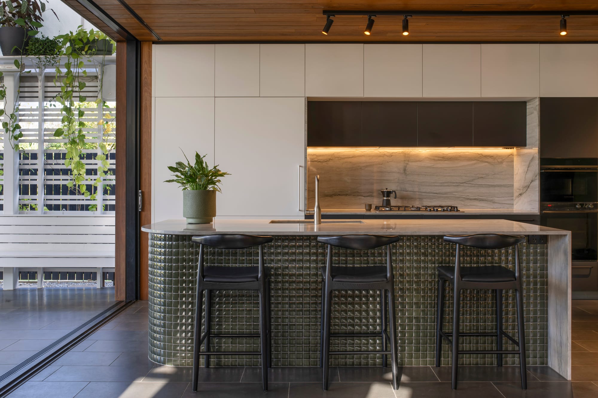 Cornerstone by Loupe Architecture. Photography by Alanna Jayne McTiernan. Kitchen with green textured tile island bench and quartzite countertops and splash back. Bluestone floors and white cabinetry. 