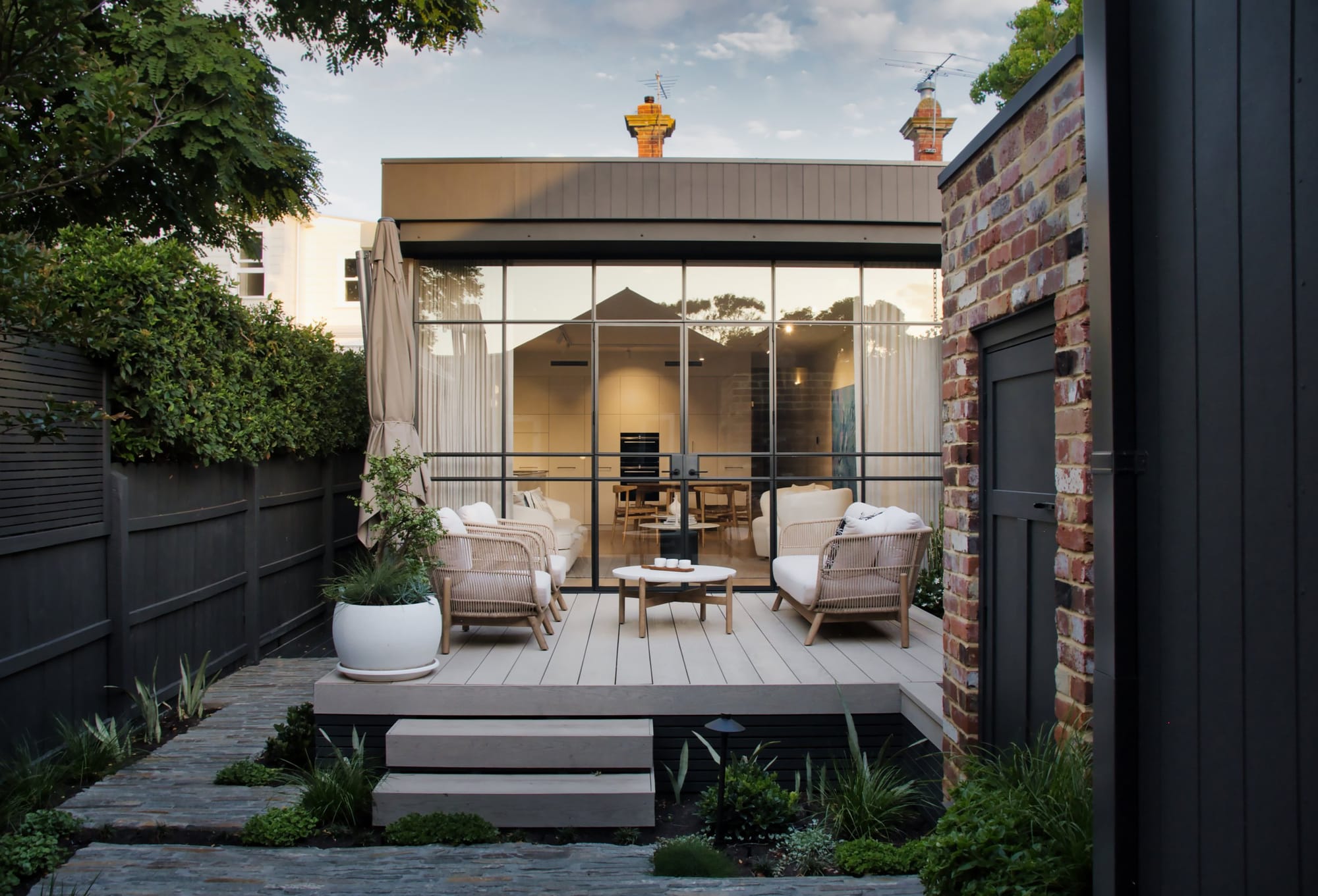 Sewell Street by ST. HELIER STUDIO. Imagery copyright of ST. HELIER STUDIO. Patio with rattan furniture in front of full length glass windows. 