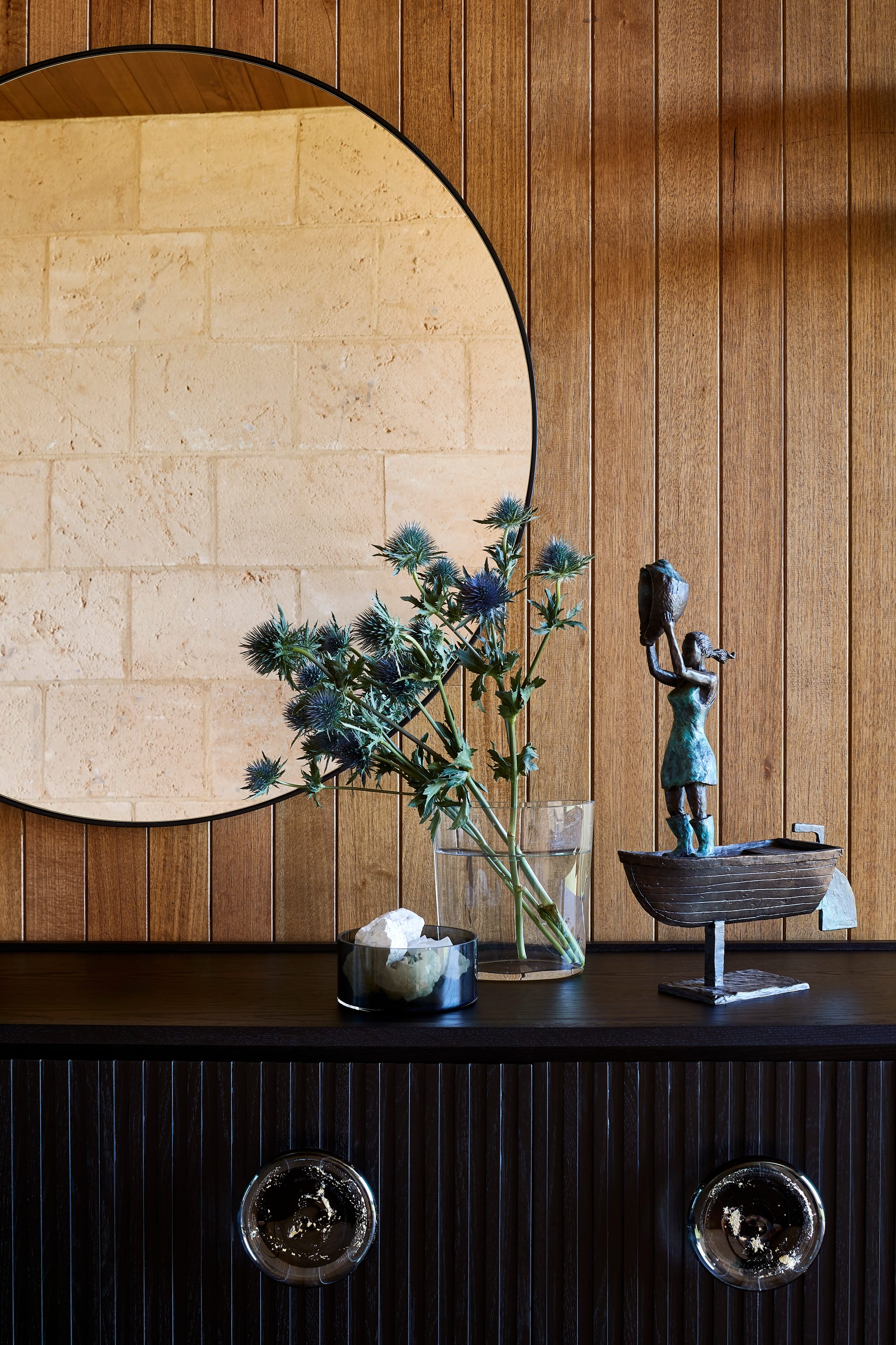 Tasmanian Timber in Flinders Residence by Abe McCarthy. Photography by Shannon McGrath. Vertical timber clad wall behind circle wall mirror, hug above dark timber vintage side board.