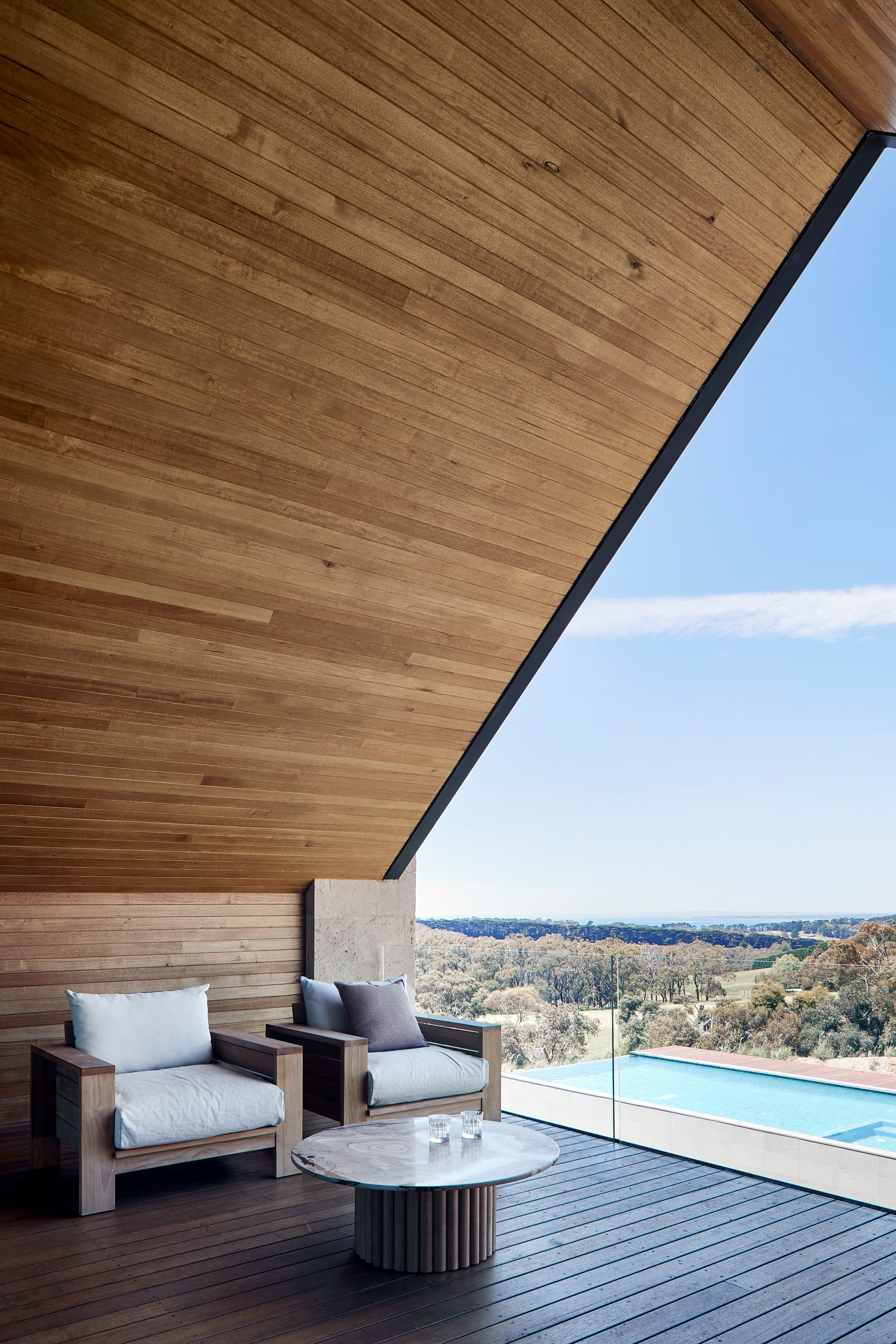 Tasmanian Timber in Flinders Residence by Abe McCarthy. Photography by Shannon McGrath. Angled timber clad ceiling on outdoor balcony extends from timber clad wall and dark timber floor.