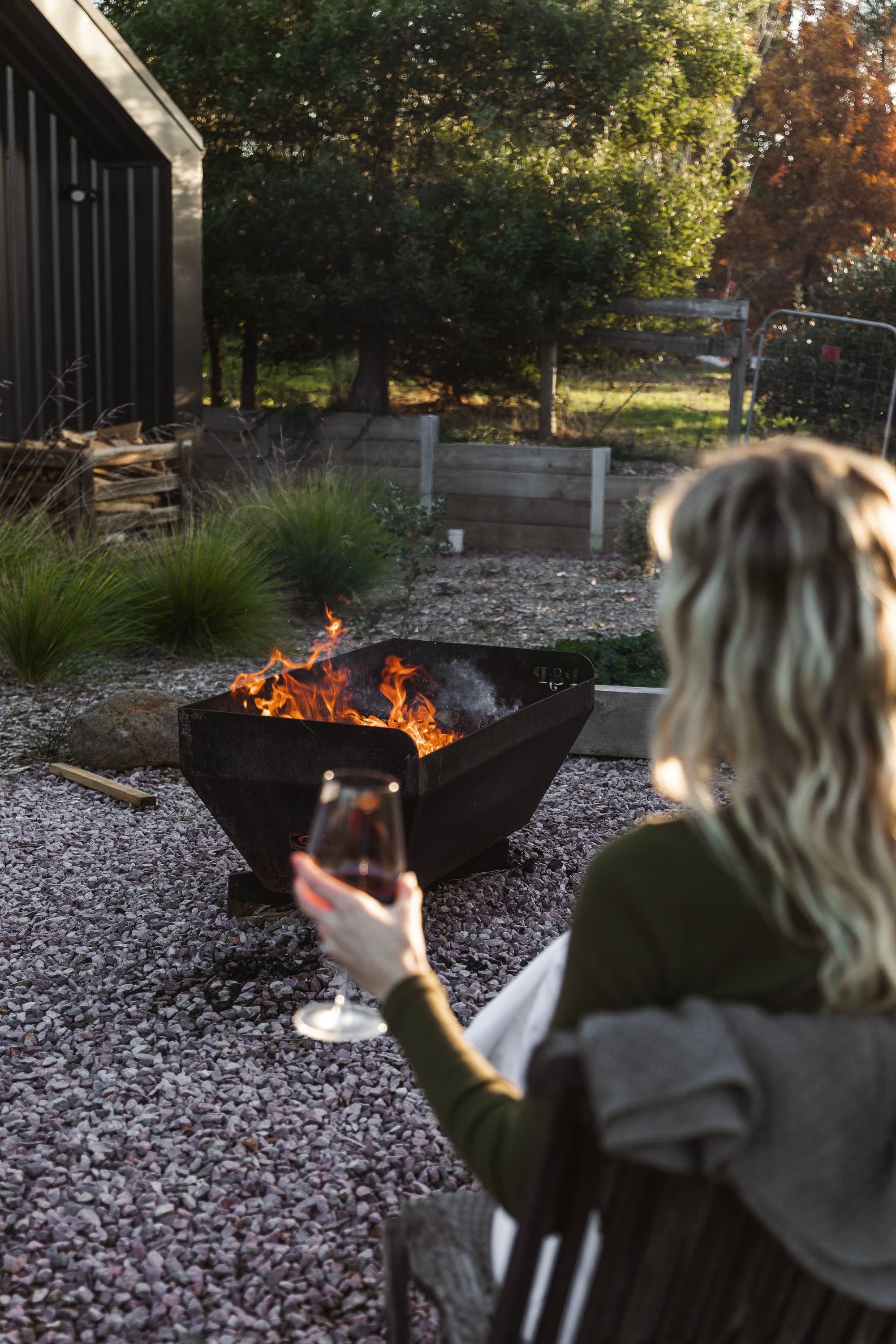 Forrest Haus Retreat. Images copyright of Forrest Haus Retreat. Woman sitting with wine on front of outdoor firepit on gravel floor. 