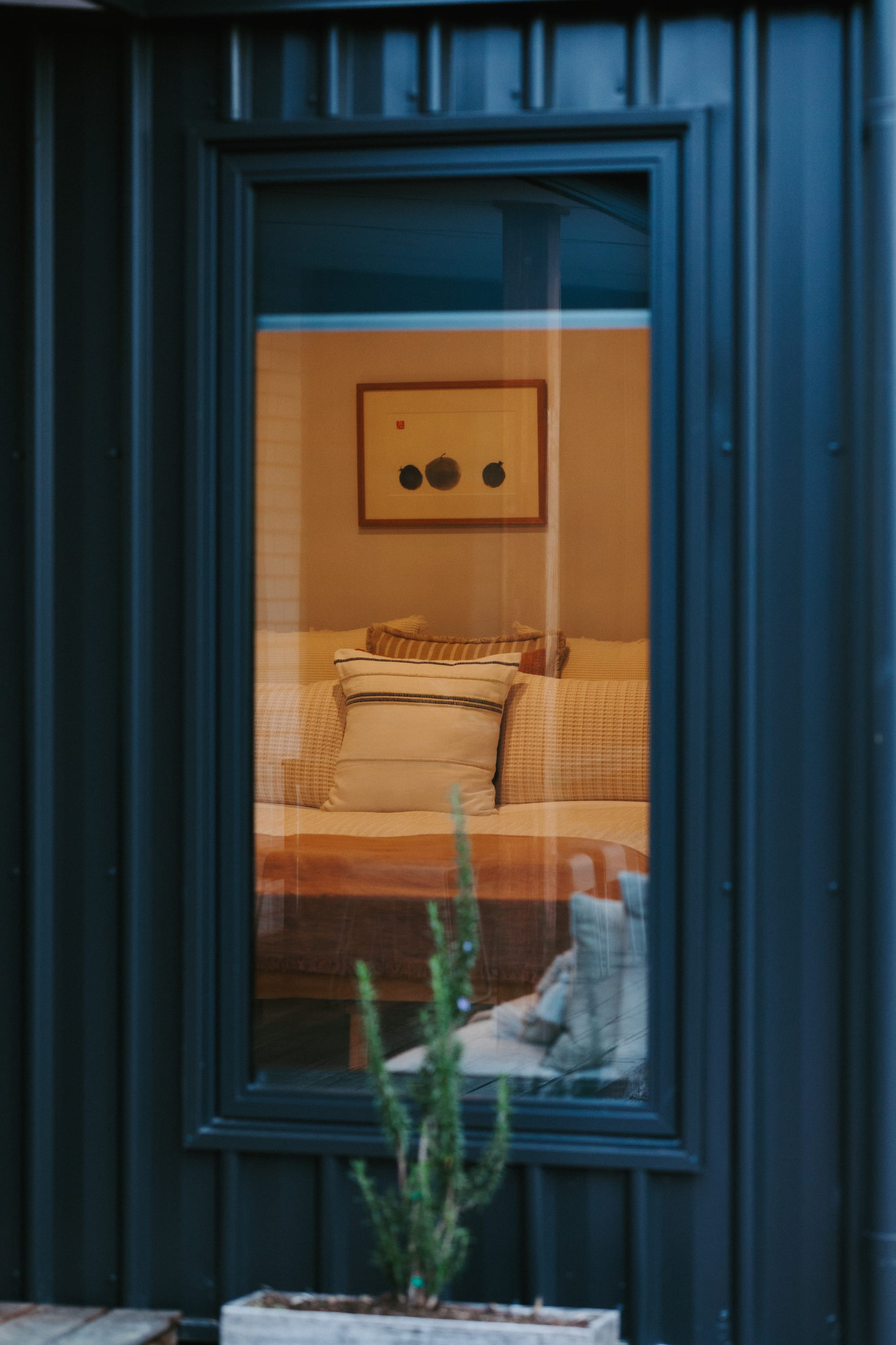 Forrest Haus Retreat. Images copyright of Forrest Haus Retreat. A detail show looking through a window on the outside showing a view to the bedroom with a warm yellow light on