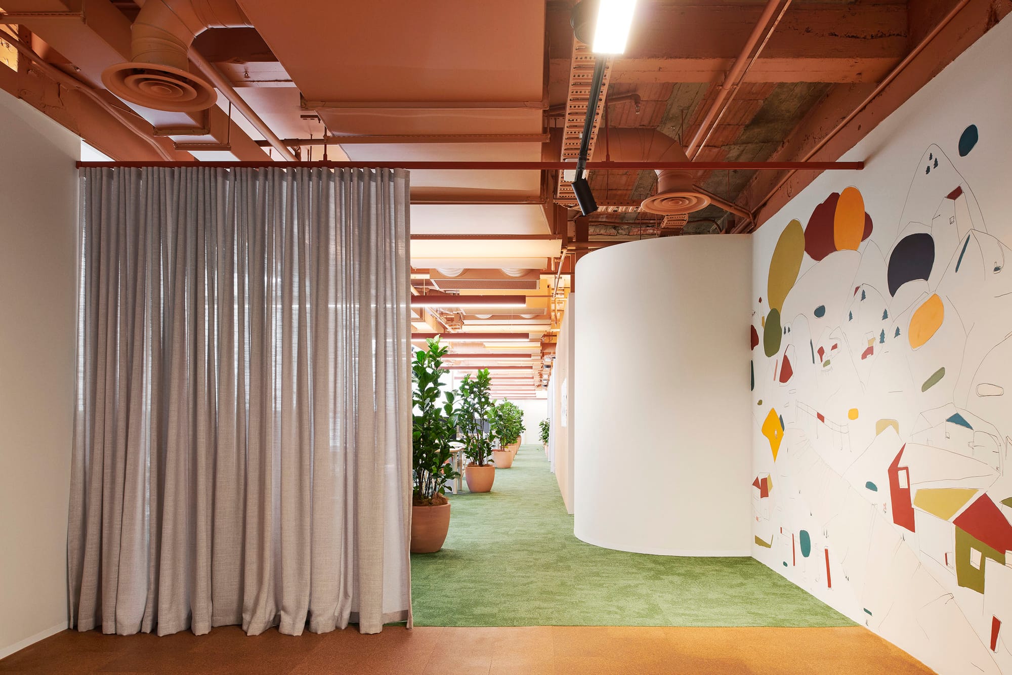 Hames Sharley Melbourne Studio by Hames Sharley. Photography by Nicole England. Mural on white wall, against green carpet and exposed terracotta ceiling. Grey curtains act as dividing wall.