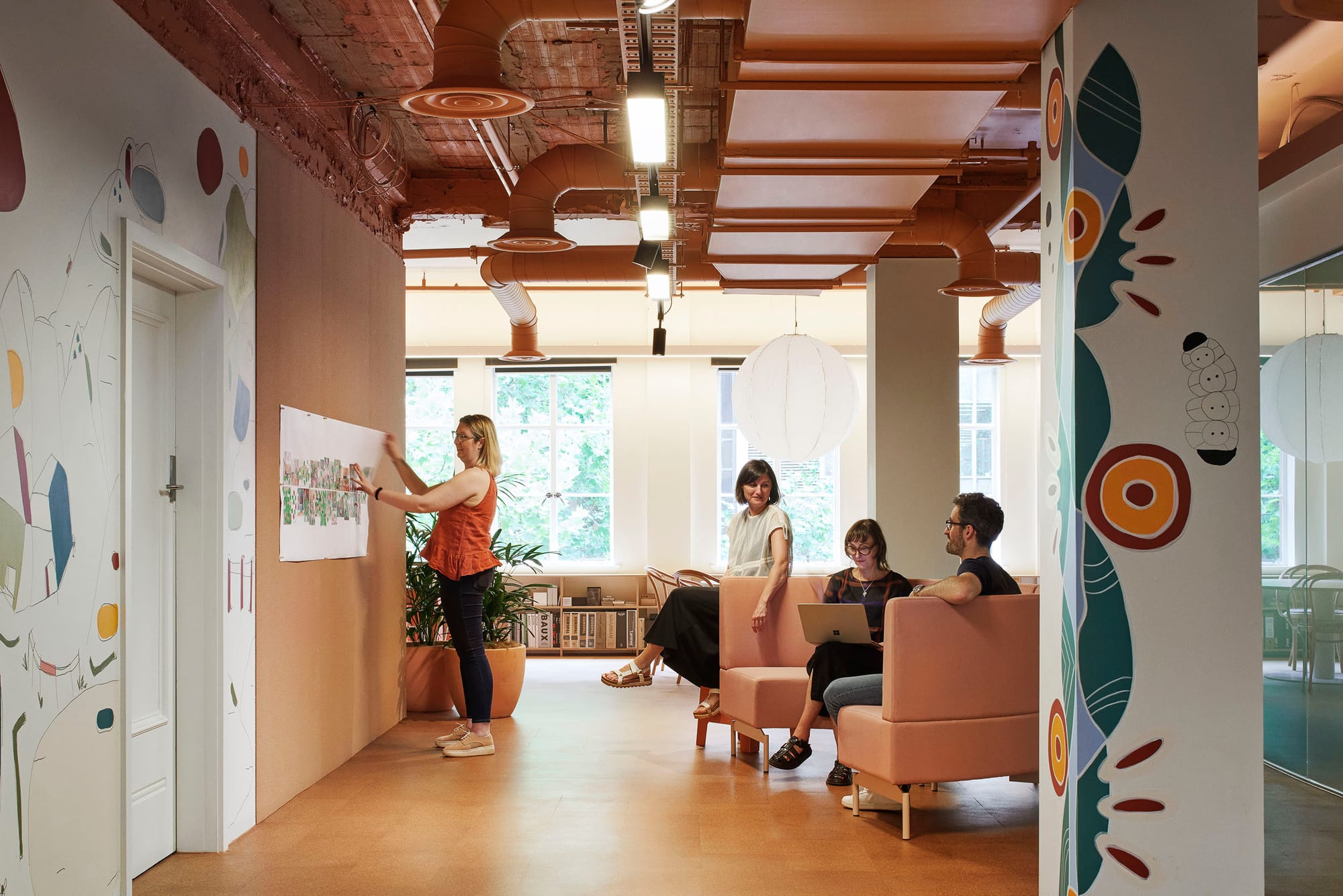 Hames Sharley Melbourne Studio by Hames Sharley. Photography by Nicole England. Office space with cork floors and terracotta exposed ceiling. Pillars and walls have coloured paintings on them. 