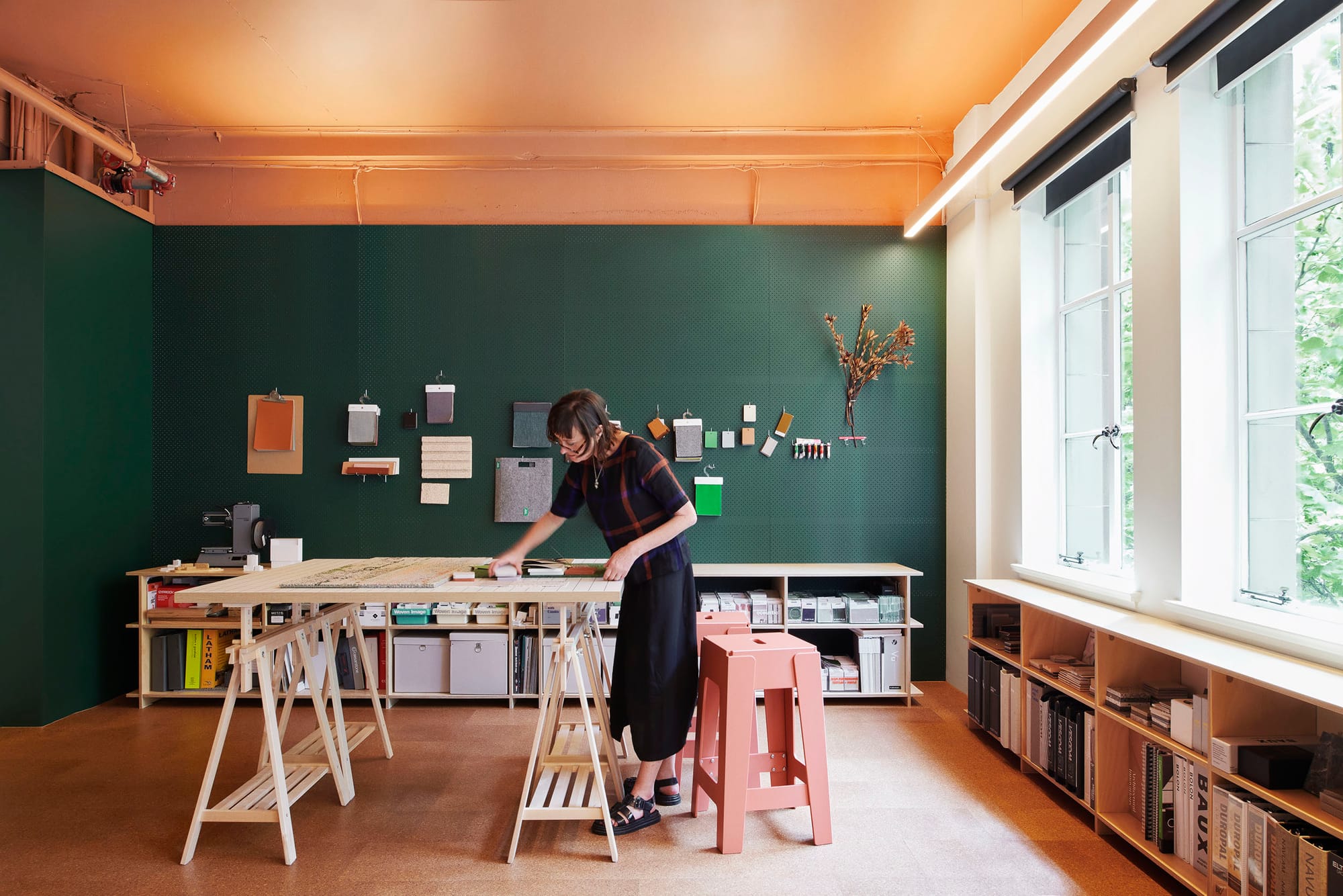 Hames Sharley Melbourne Studio by Hames Sharley. Photography by Nicole England. Dark green cork walls and warm cork floors. White trestle table, low bookcases and red stool. 