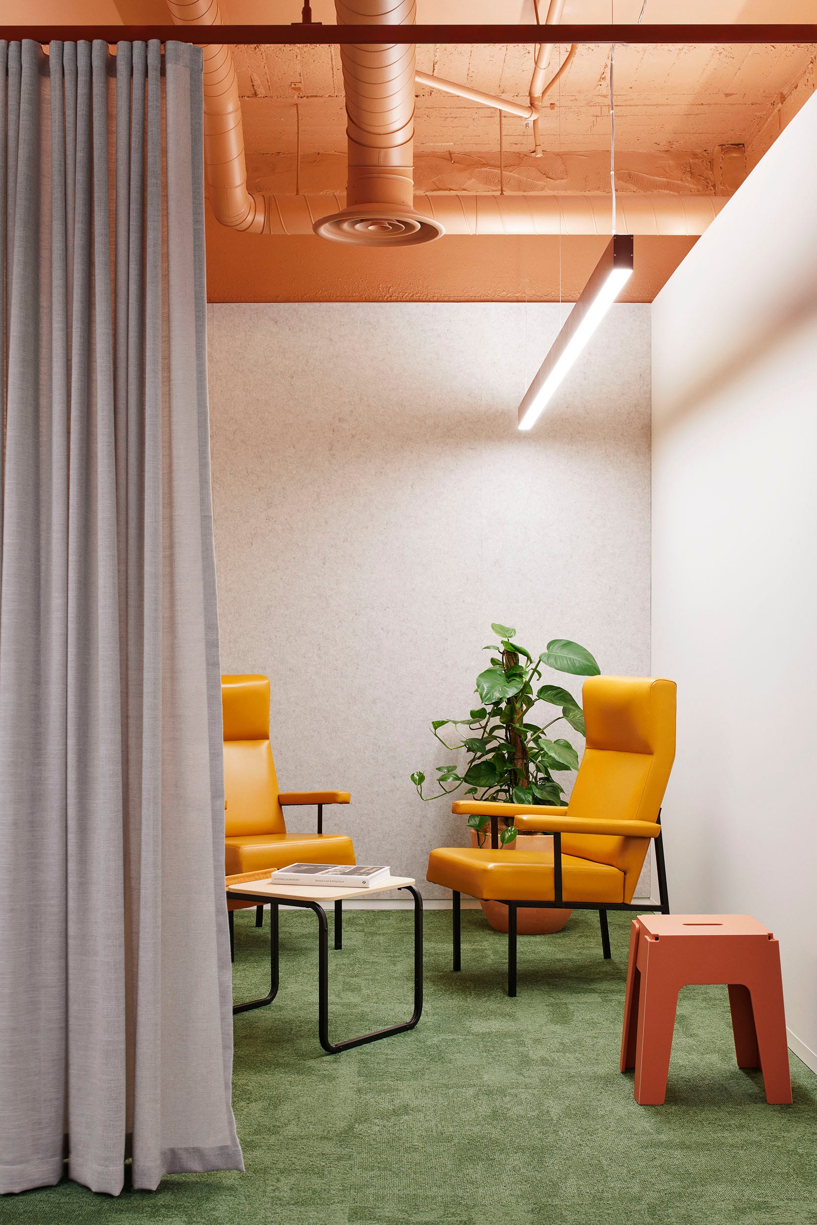 Hames Sharley Melbourne Studio by Hames Sharley. Photography by Nicole England. Office space with mossy green carpets, yellow leather armchairs, red stools, terracotta exposed ceiling and grey walls. 