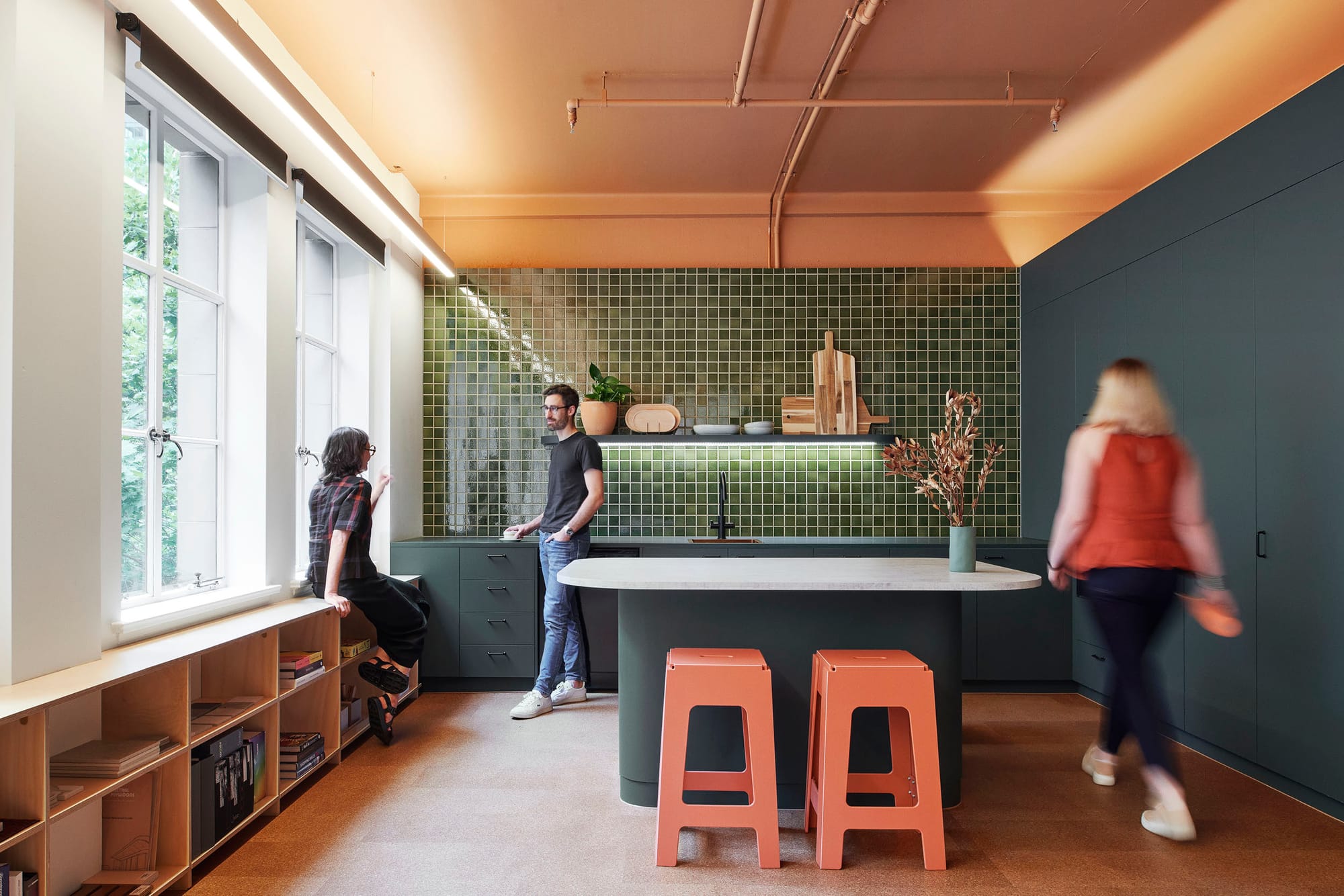 Hames Sharley Melbourne Studio by Hames Sharley. Photography by Nicole England. Office kitchen space with dark green mosaic tiled wall and dark teal cabinetry. Cork floors and terracotta exposed ceiling.