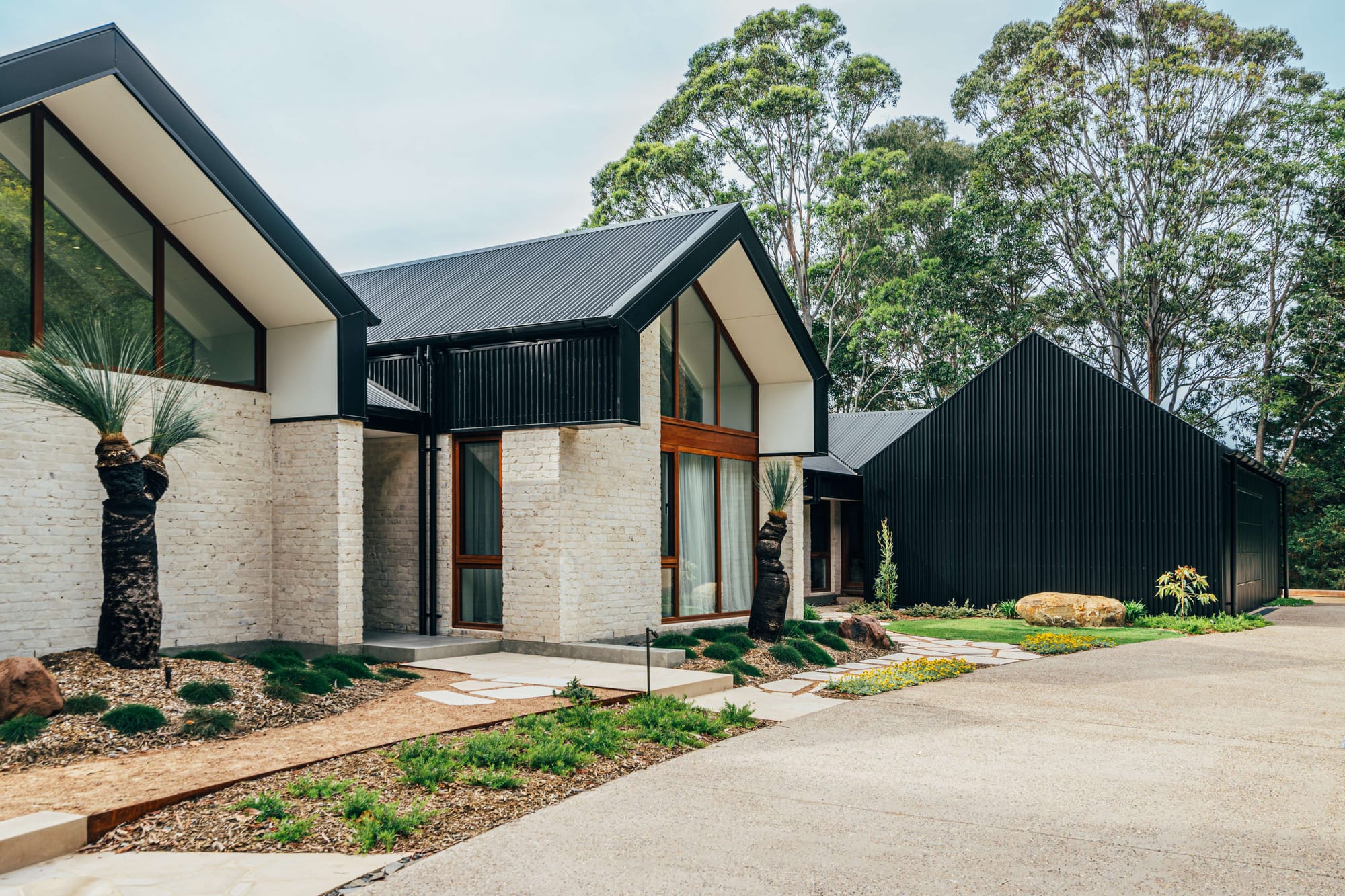 Project 465 by Robertson Collectif. Photography by Anna Mul. Facade and driveway of rural home with black gabled roof and light stone brick walls.