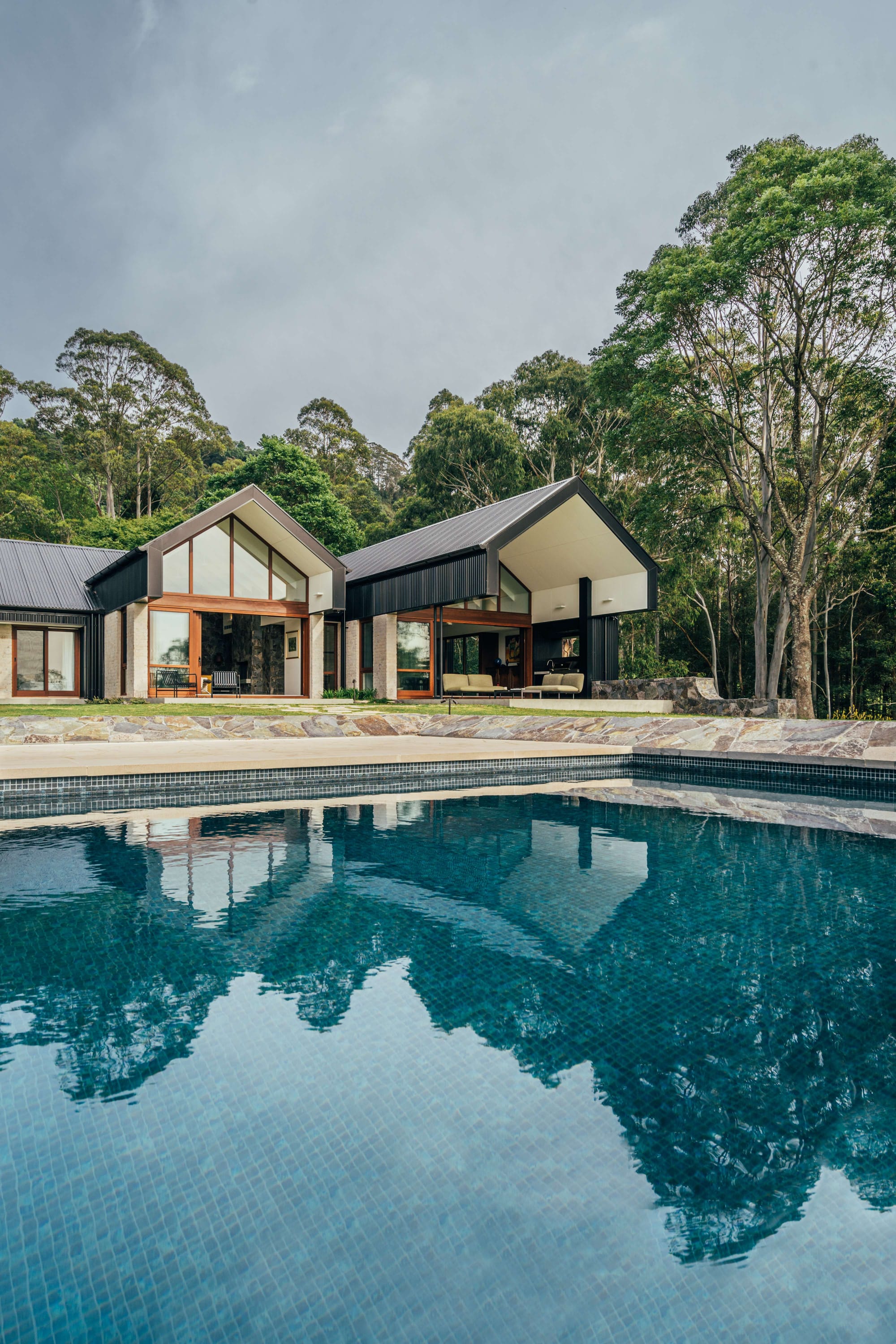 Project 465 by Robertson Collectif. Photography by Anna Mul. Rear facade of home with large tiled pool in foreground. Gabled roof and patio.