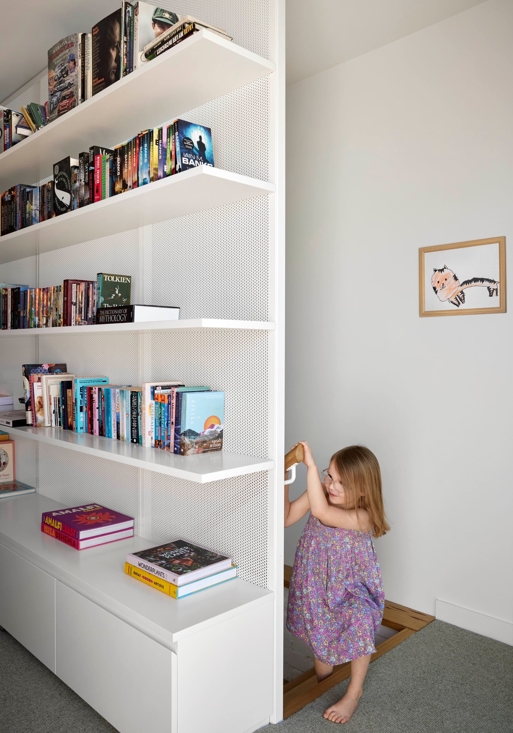 Rosie by Eckersley Architects. Photography by Tess Kelly. White integrated bookshelf in hallway with grey carpets. Timber staircase leading up from ground floor. 