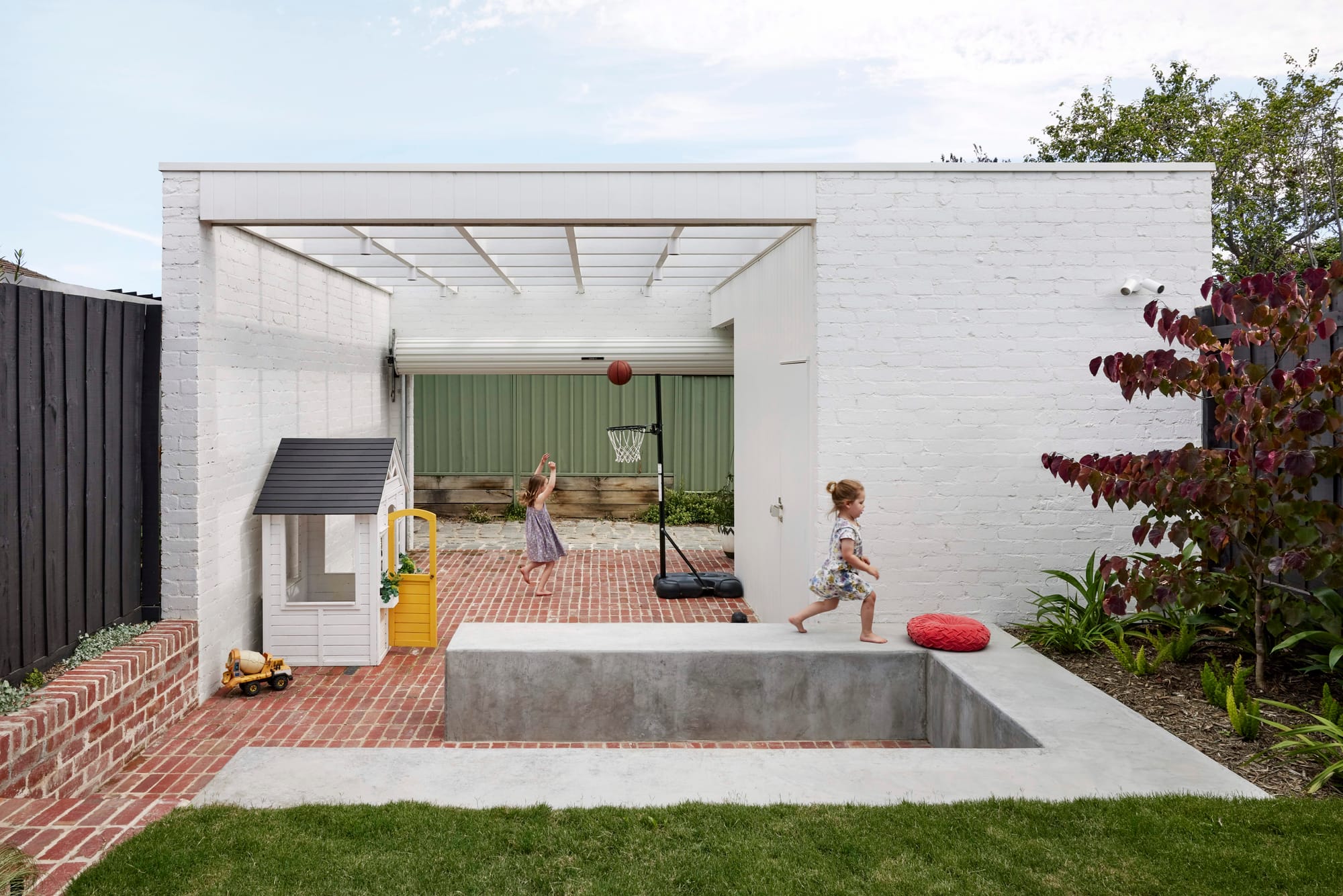 Rosie by Eckersley Architects. Photography by Tess Kelly. Sunken outdoor entertaining zone with brick floors and concrete retaining walls. White brick structure.