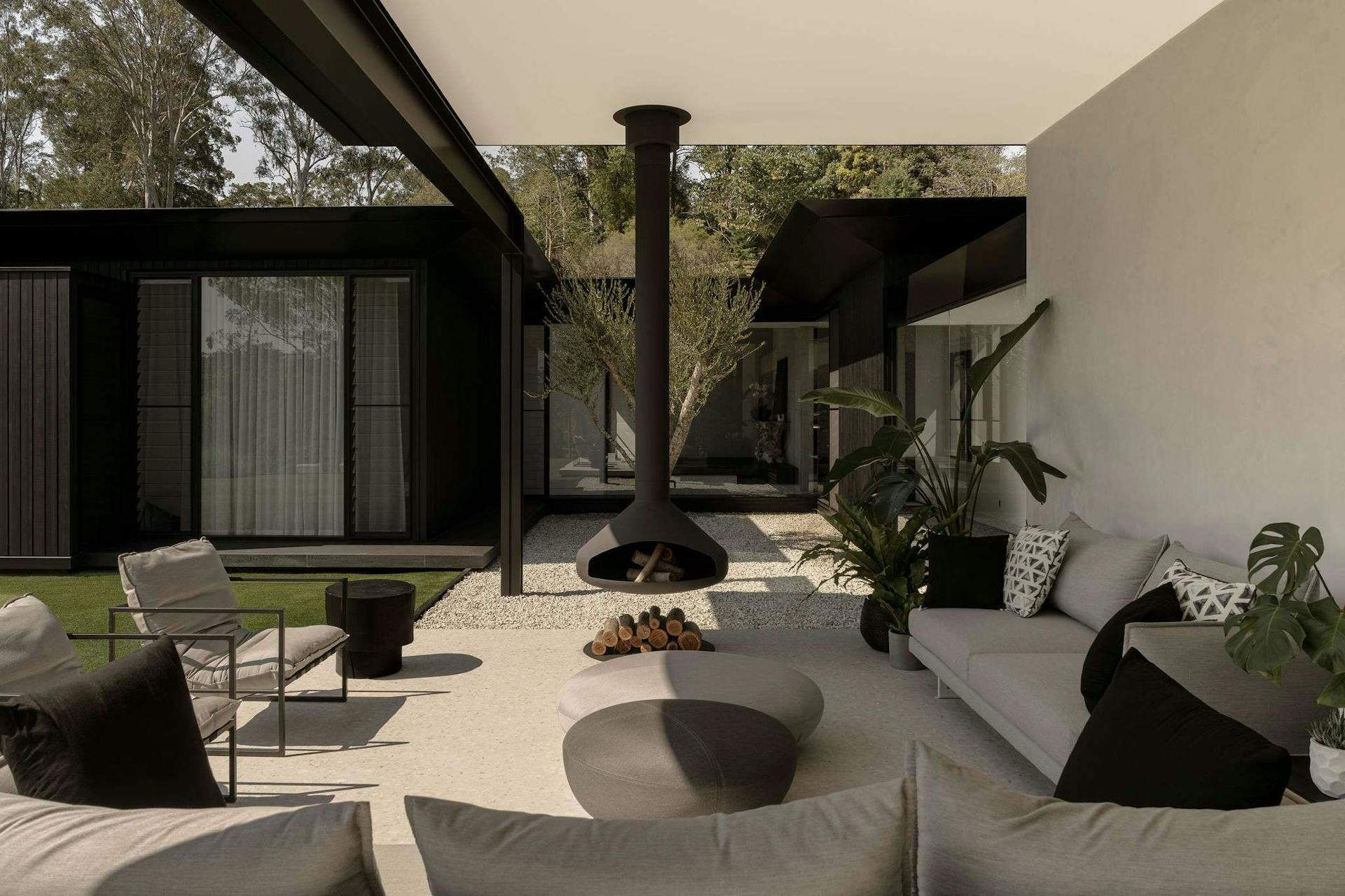 Blackwood Doonan by Sarah Waller Architecture. Photography by Alyne Media. Outdoor living area with freestanding black fireplace and grey sofas.