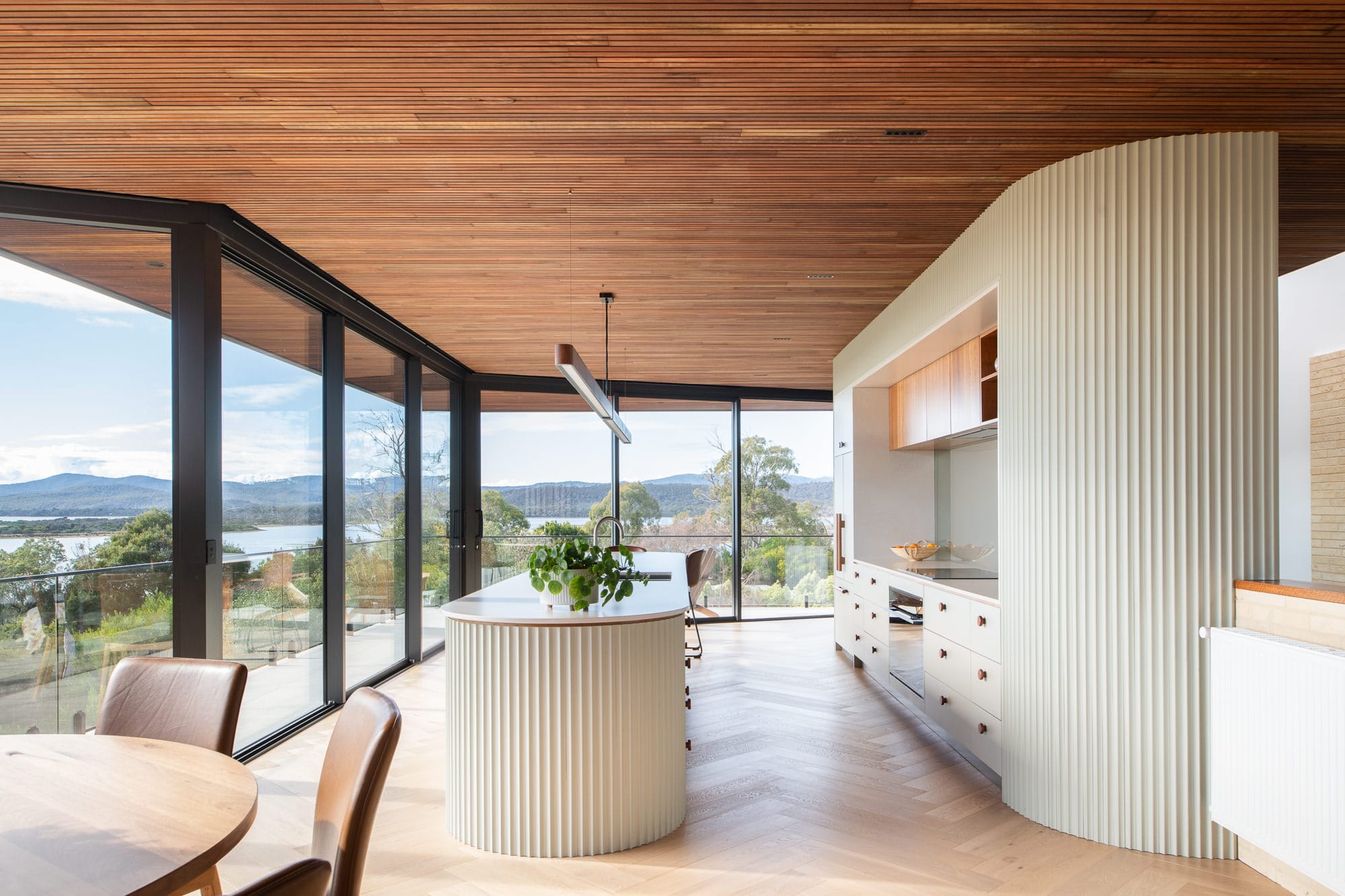 Mortlock Timber Series: The Milldam. Photography by Anjie Blair. Hallway with light timber herringbone floors, dark timber clad walls, and a large open void with rubber plant growing in gap. 