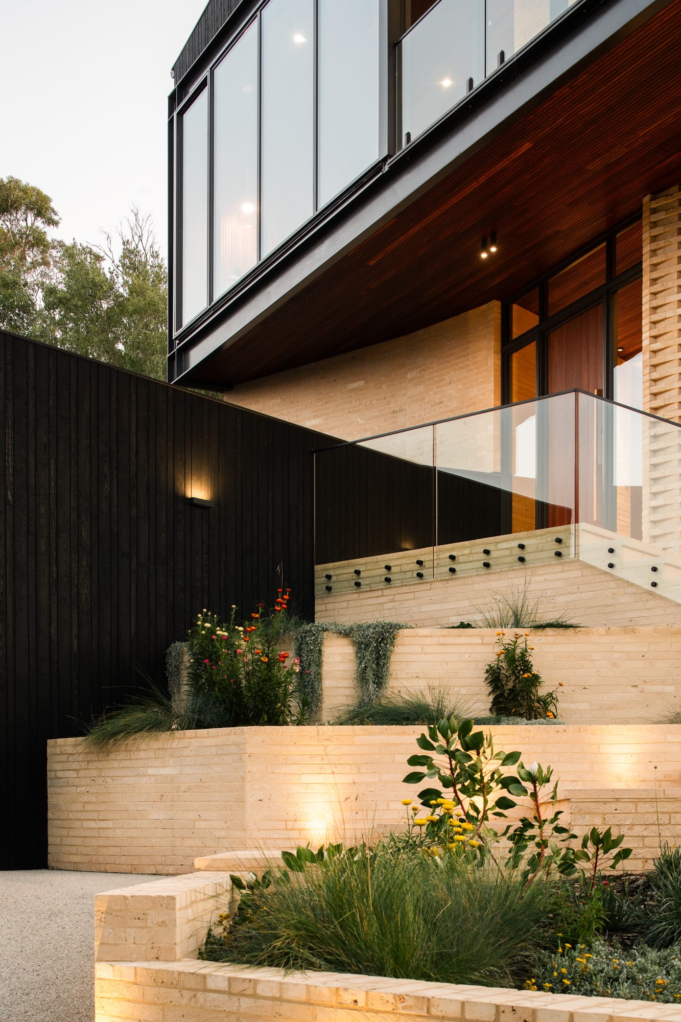 Mortlock Timber Series: The Milldam. Photography by Anjie Blair. Open plan kitchen and living space with white cabinetry and lounge, timber clad ceilings and timber herringbone floors. Floor-to-ceiling windows overlooking bushland. 