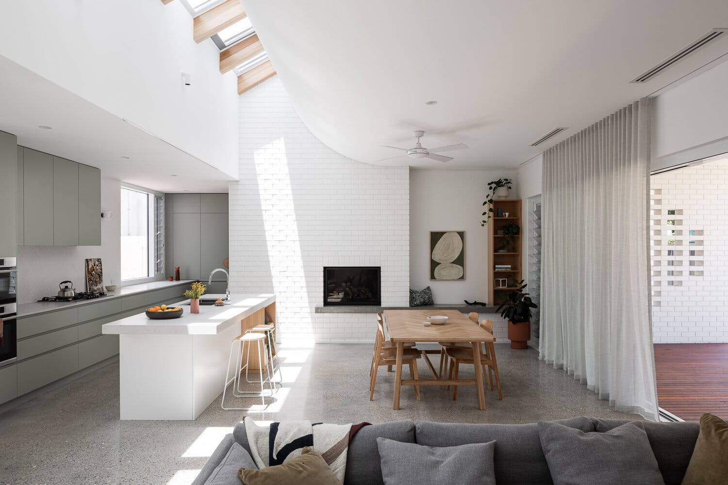 The Third by Dalecki Design. Photography by Dion Robeson. High curved celing into skylight over open plan living, dining and kitchen space with polished concrete floors and white brick walls. 