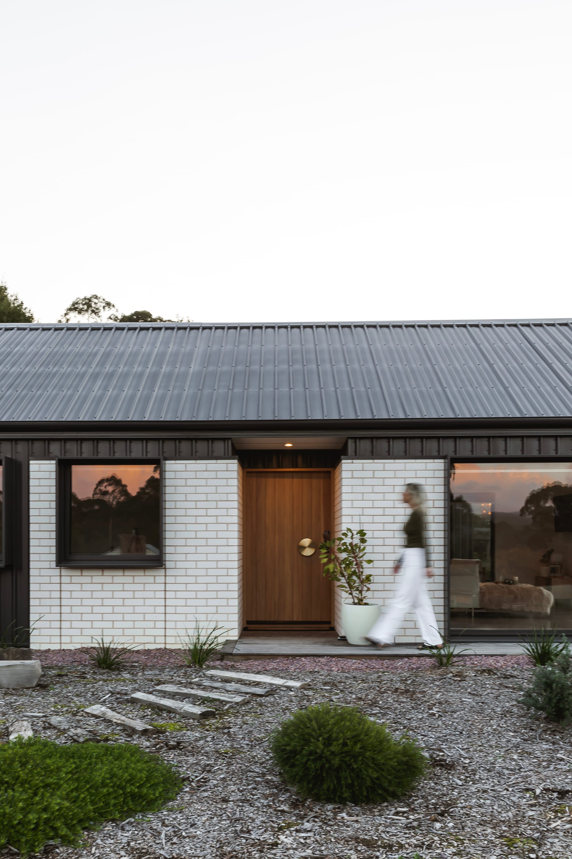 An external shot of the front door of Forrest Haus Retreat with a woman walking and scattered landscape in the foreground