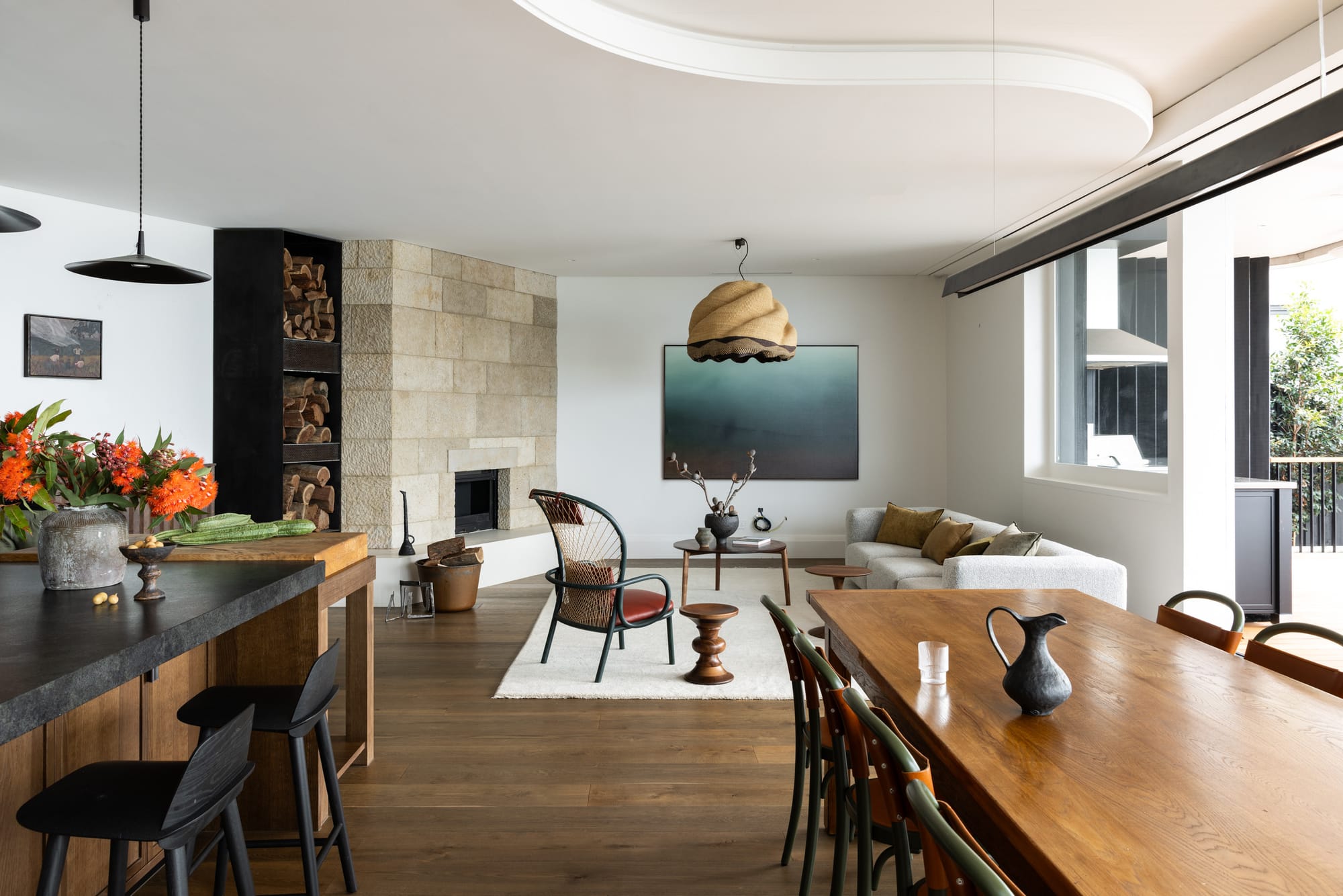 Ripple House by Marker Architecture. Living room with view on dining table, kitchen counter and couch with chimney.