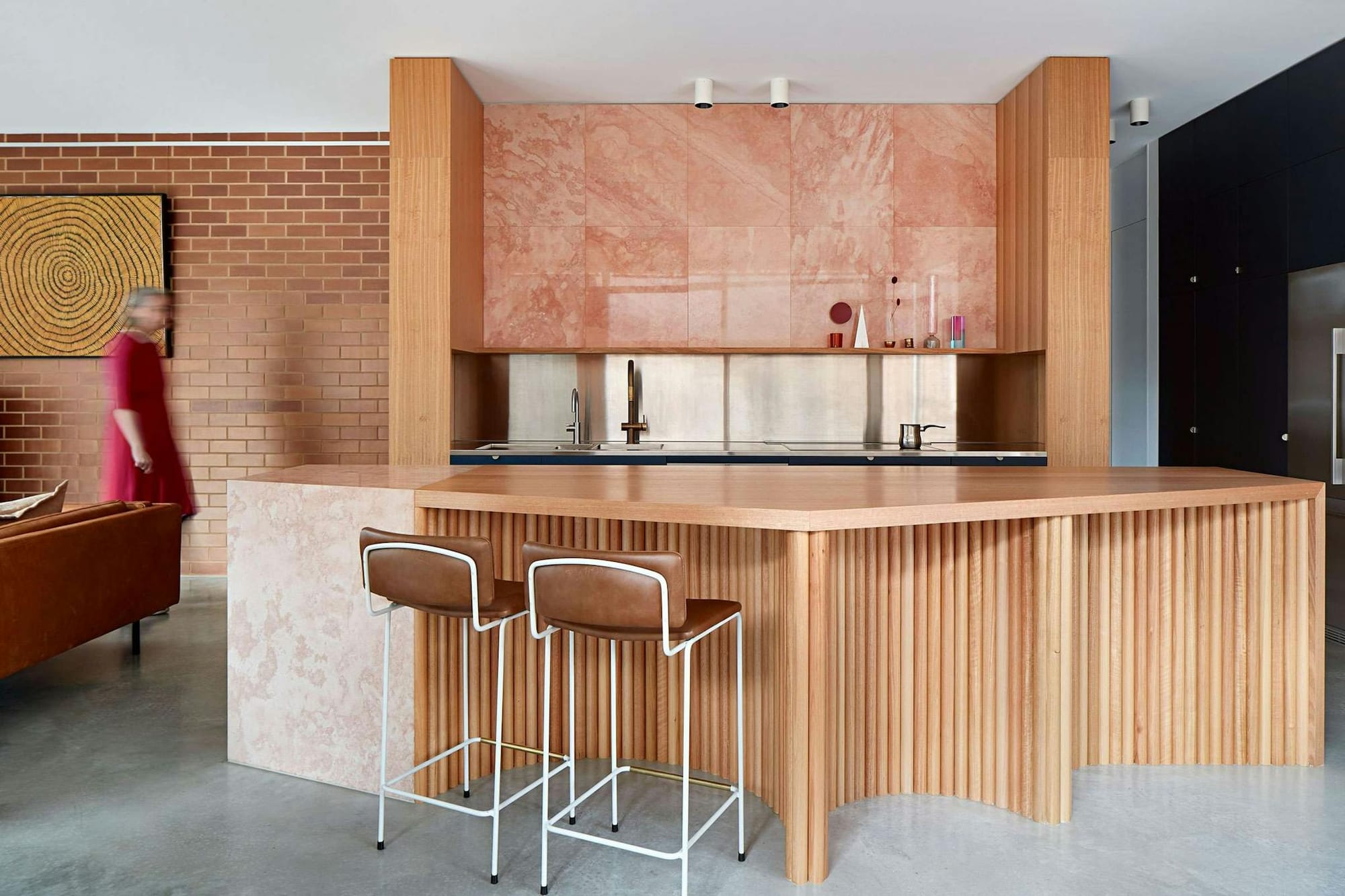 Merri Creek by WOWOWA. Stainless steel kitchen featuring pine wooden, beige travertine island, orange marble and brick wall.