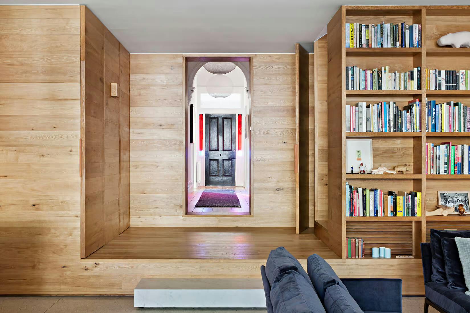 Victoria Gardens House by Lucy Clemenger Architects. Living room with entrance view featuring oak wood, frame and shelving installation.