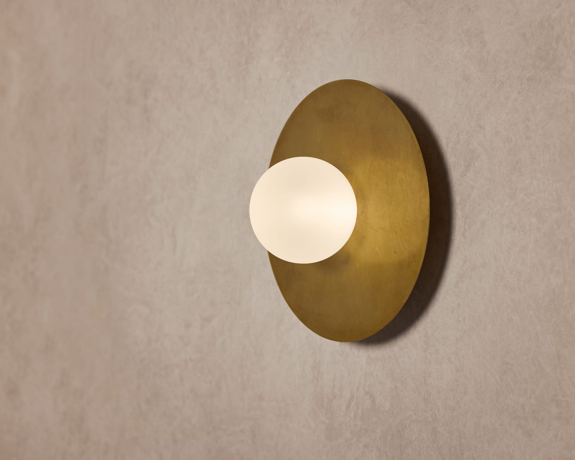 A detail shot of a brass wall light by the Melbourne brand alt. Artefact with the round light turned on.