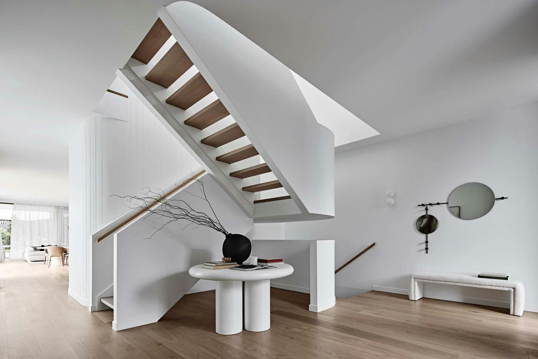 Amiri Courtyard House by Keller Architects. Hallway with white, curved free hanging staircase and view to living room.