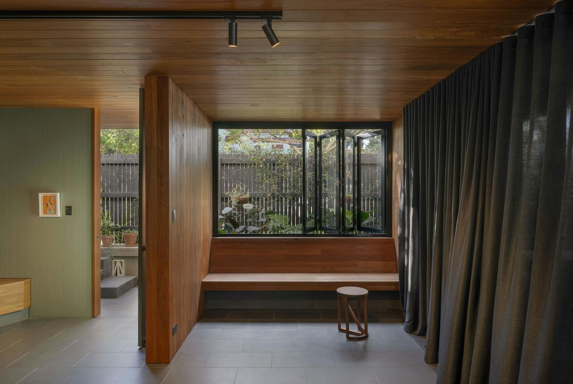 Cornerstone by LOUPE Architecture. Living space featuring wood panel ceiling and walls, floor to ceiling curtains and view to garden.