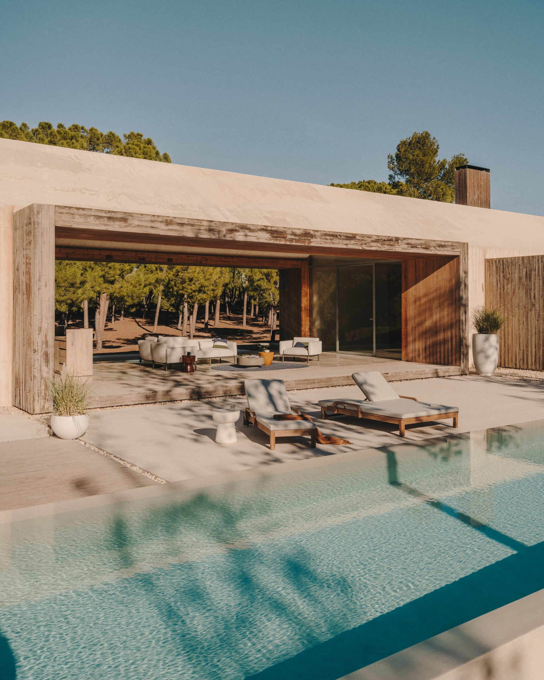 Kave Home. Pool overview to lougers and roofed outdoor area with seating facilities surrounded by nature.