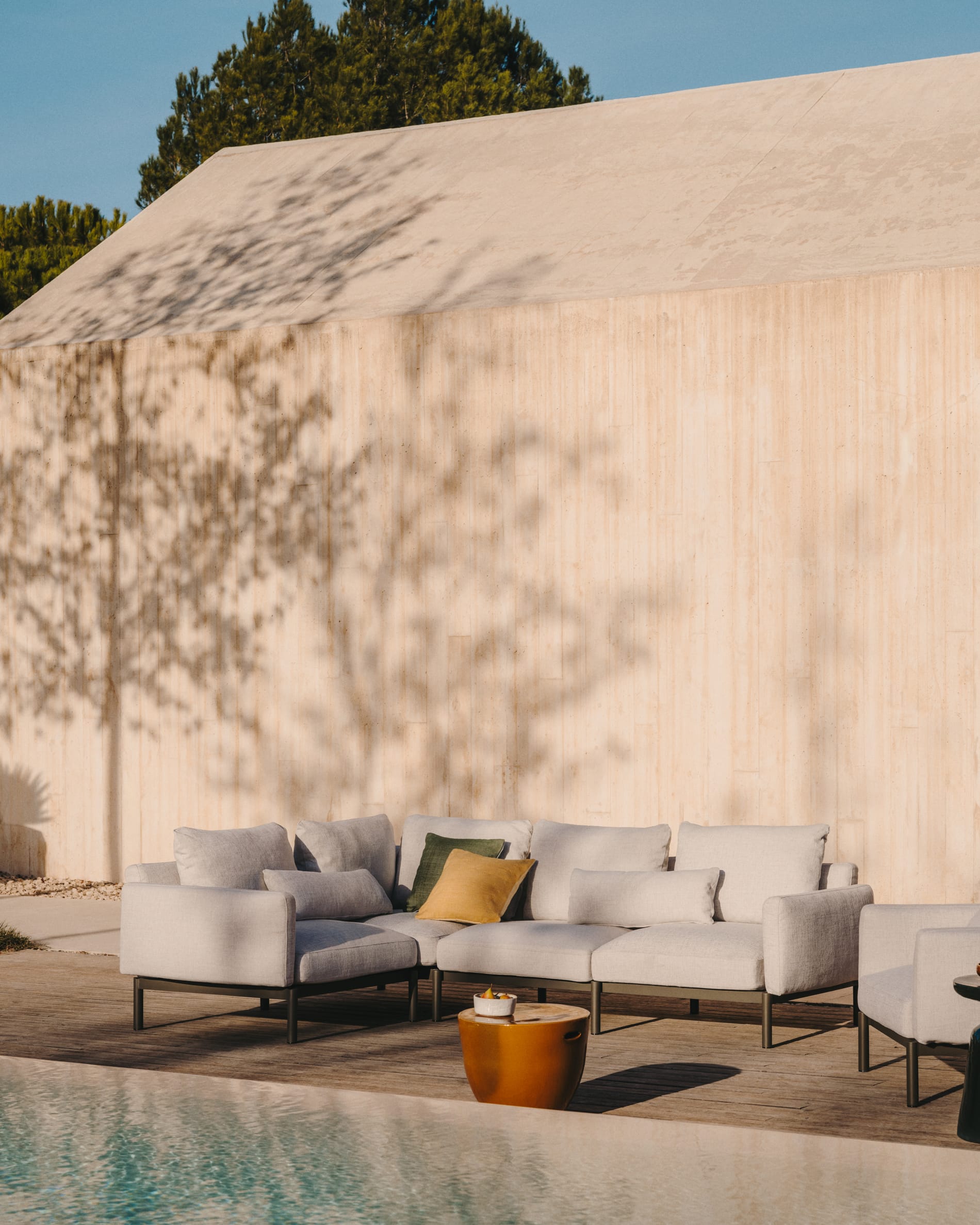 Kave Home. Beige outdoor fabric sofa by the pool with orange varnished coffee table.