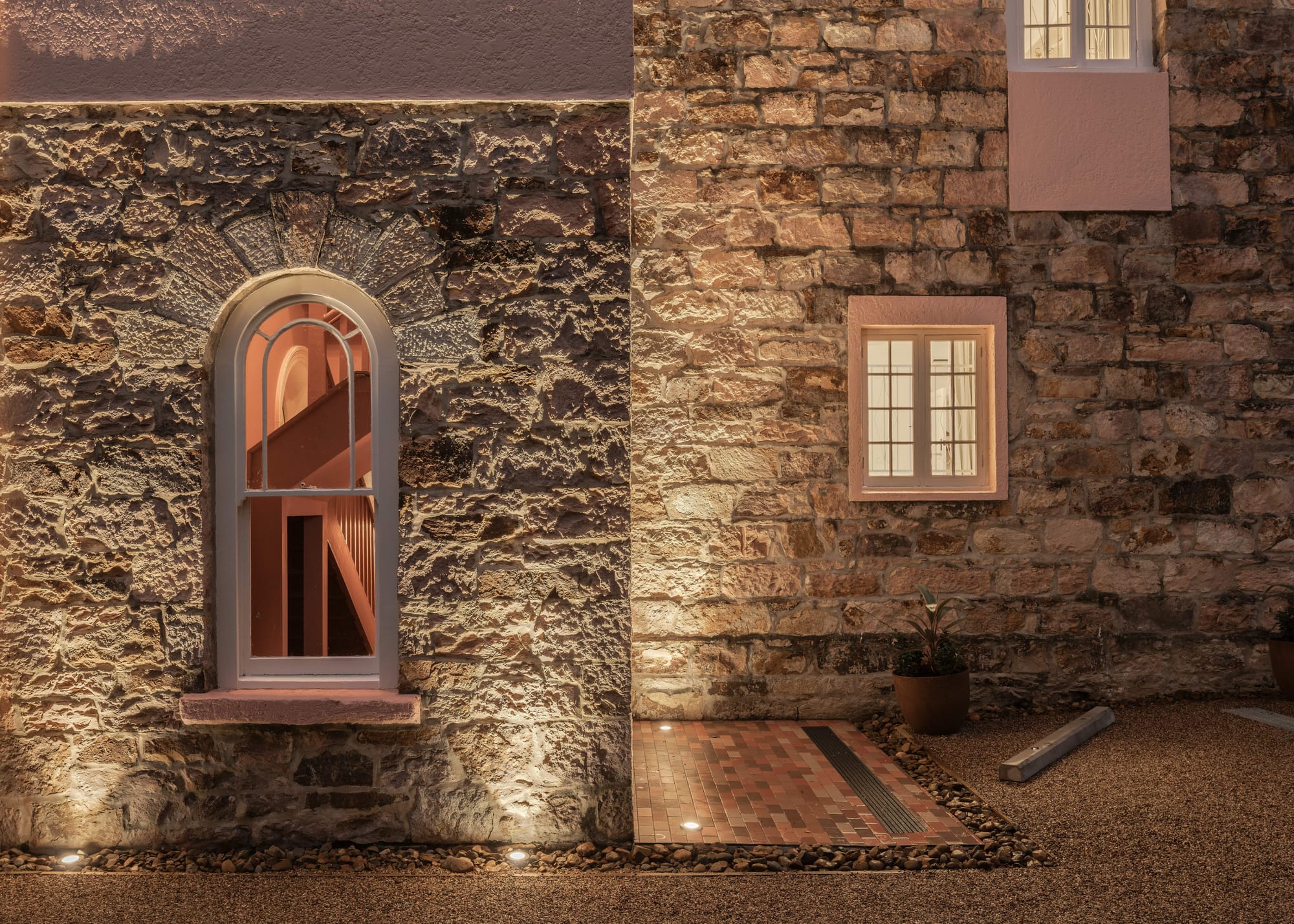 An exterior shot of Miss Midgleys showing the sandstone walls and warm light of the interiors through the heritage windows