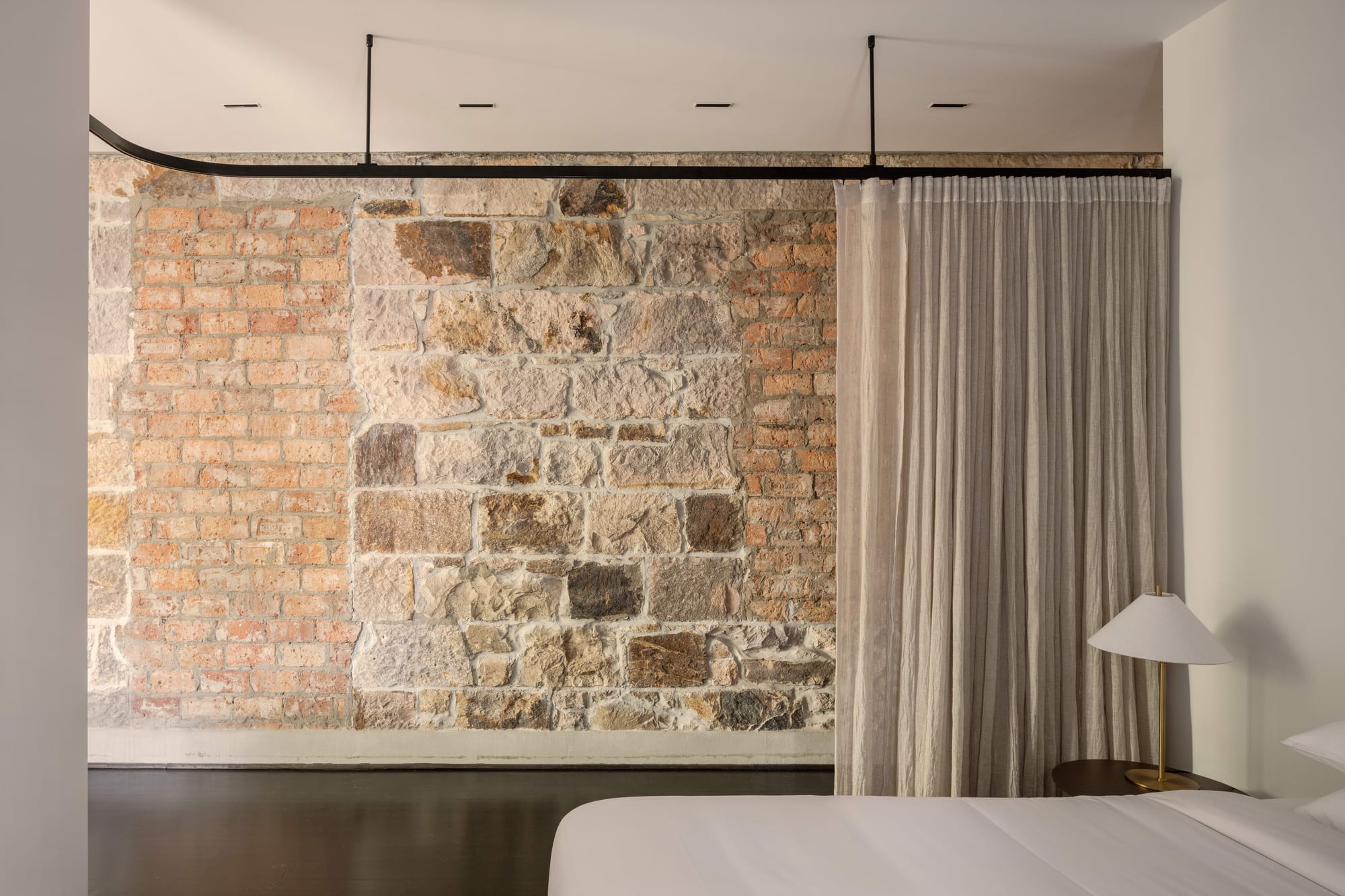 An interior shot of a Miss Midgley hotel room showing the bedroom space with a linen curtin and sandstone wall in the background