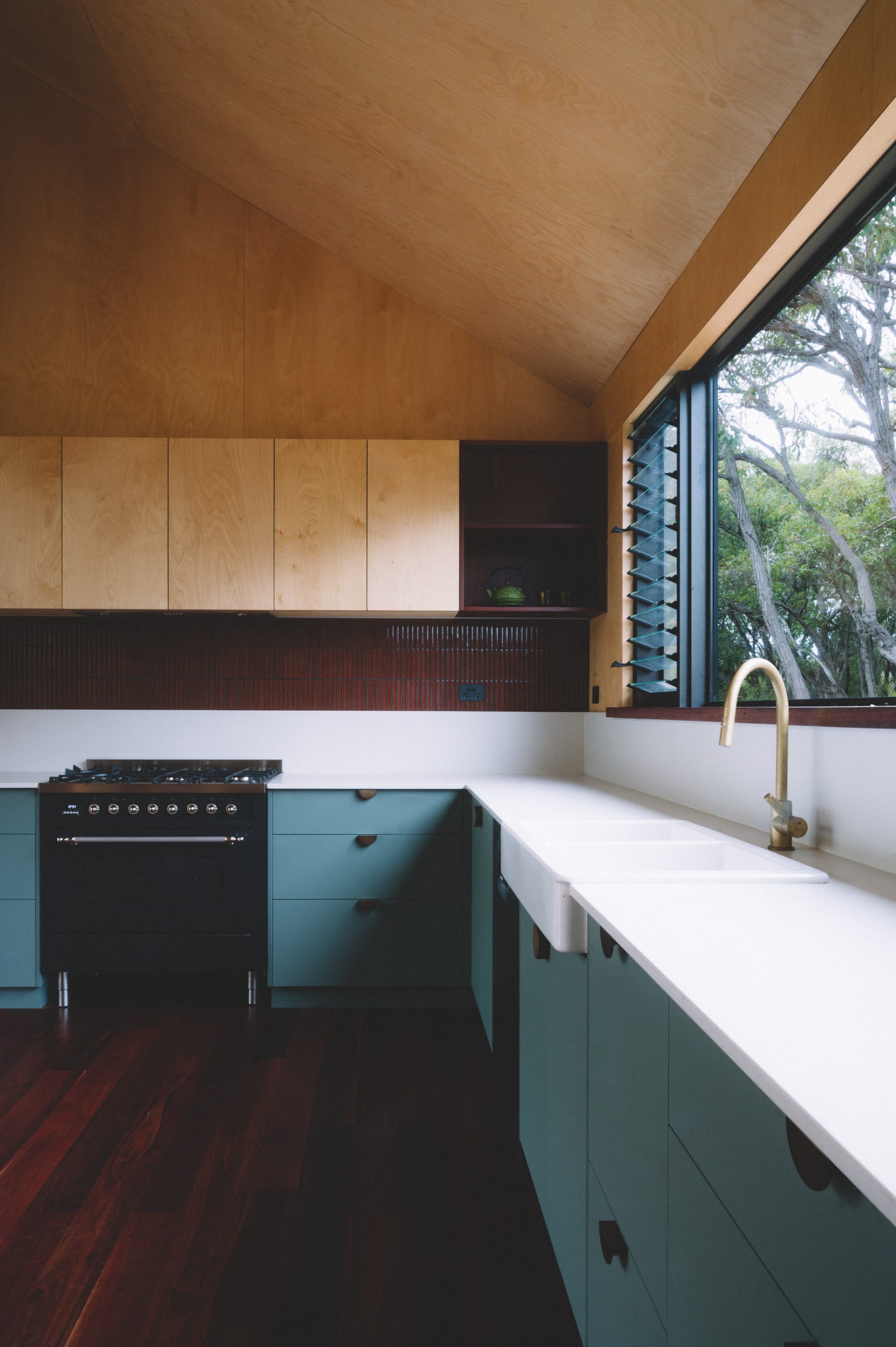 Nullaki House by Bare Architects. Fitted kitchen featuring plywood and sage green cabinets and view to nature.