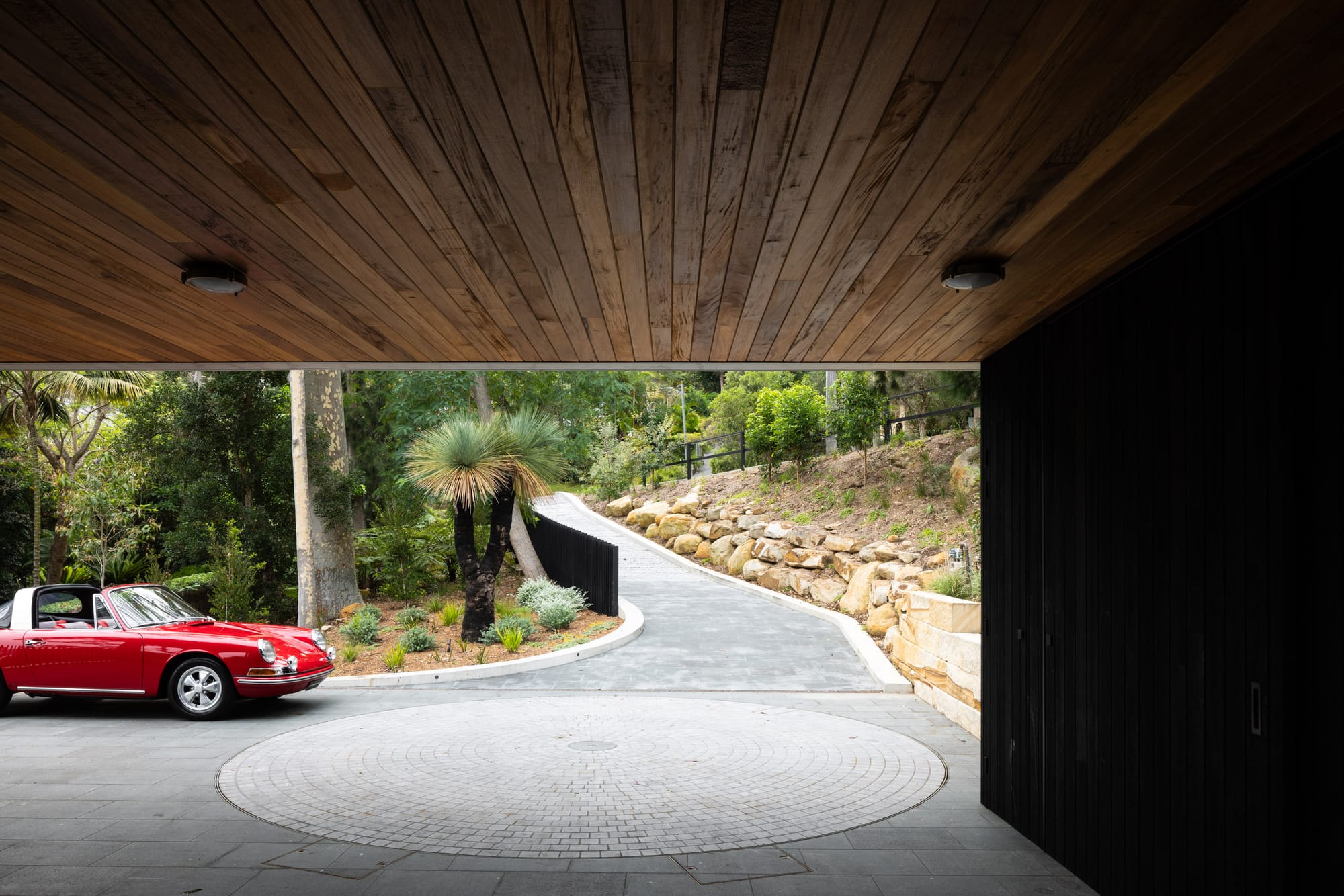 Ripple House by Marker Architecture. Driveway with red Porsche surrounded by plants and trees.