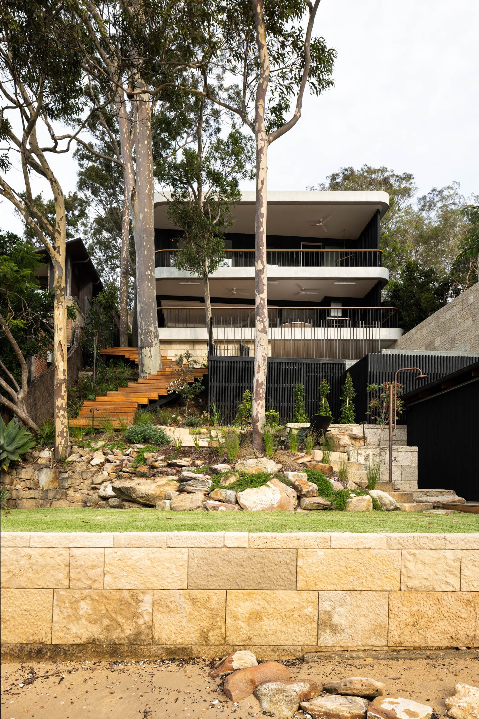 Ripple House by Marker Architecture. House at the beach featuring outdoor shower and wooden staircase, surrounded by trees.