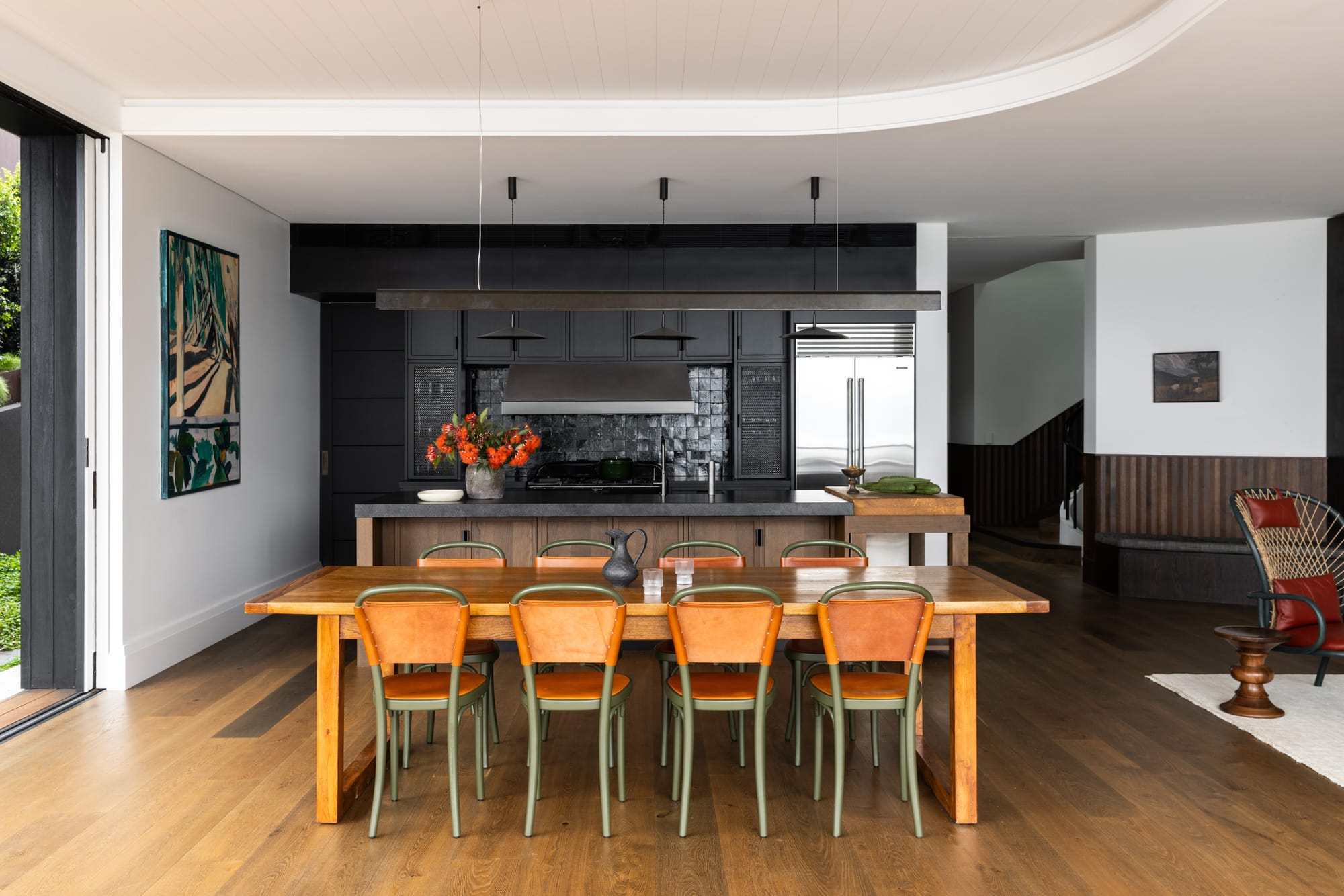 Ripple House by Marker Architecture. Black kitchen with wooden dining table and suspended ceiling.