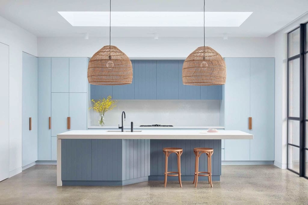 The Unbricked House by Merrylees Architecture. Kitchen area featuring blue painted, wood panel kitchen island and white worktop and blue, fitted cabinets.