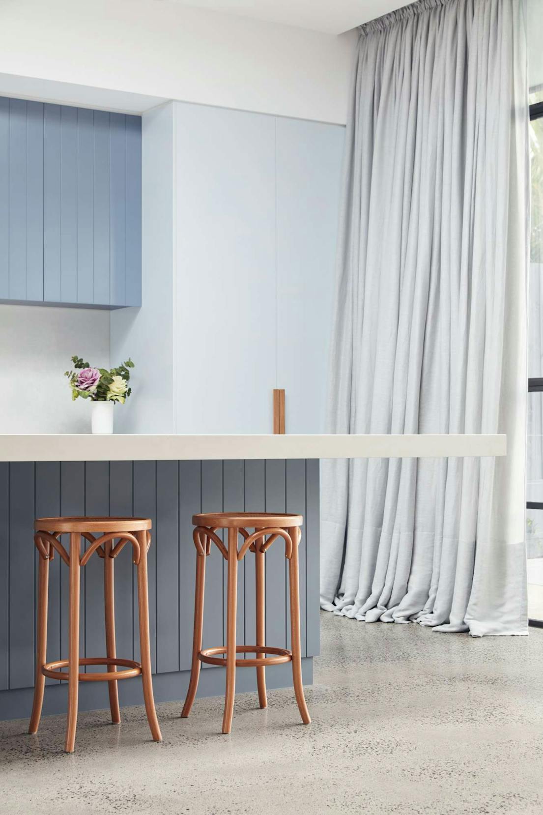 The Unbricked House by Merrylees Architecture. Wooden bar chairs on kitchen island, blue walls and floor to ceiling curtains.