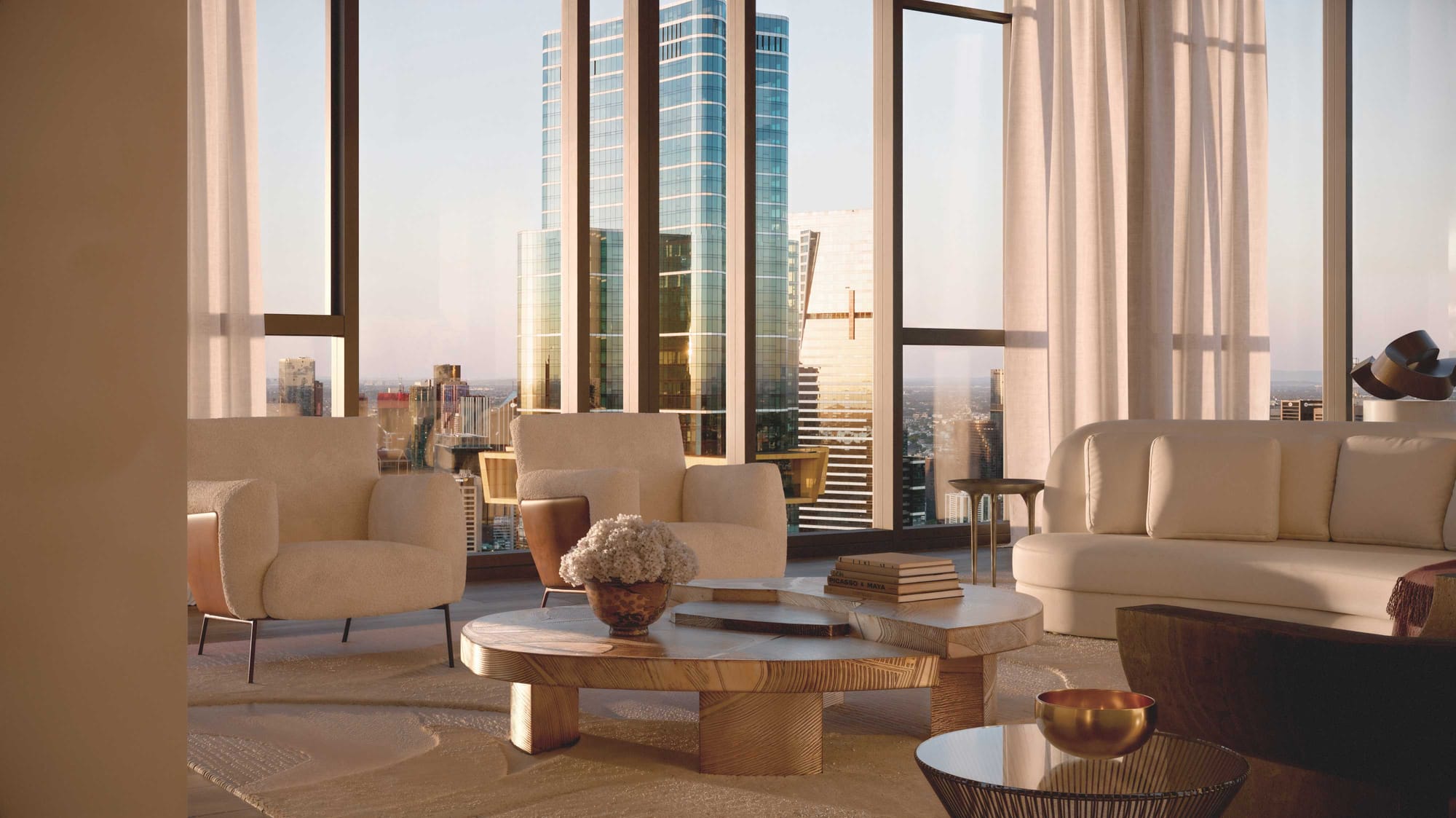 BLVD Penthouse by David Hicks. Living room featuring creme pouf sofa and armchairs with floor to ceiling windows and view on skyscraper.