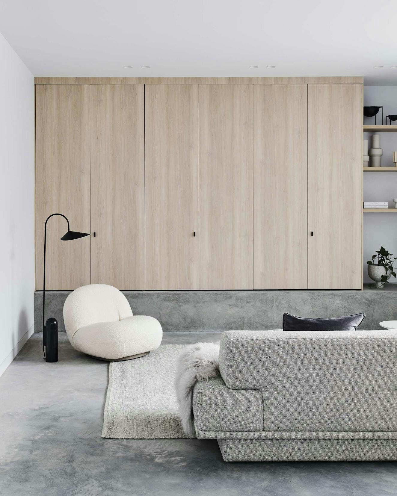 Elsterwick House by Merrylees Architects. Living room featuring light grey sofa, white pouf and wooden fitted in cabinet.