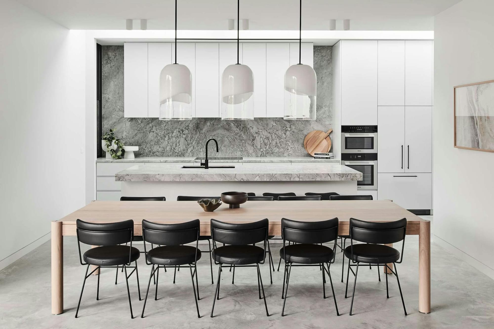 Elsterwick House by Merrylees Architects. View to grey, marble kitchen featuring seating area with wooden table and black dining chairs.