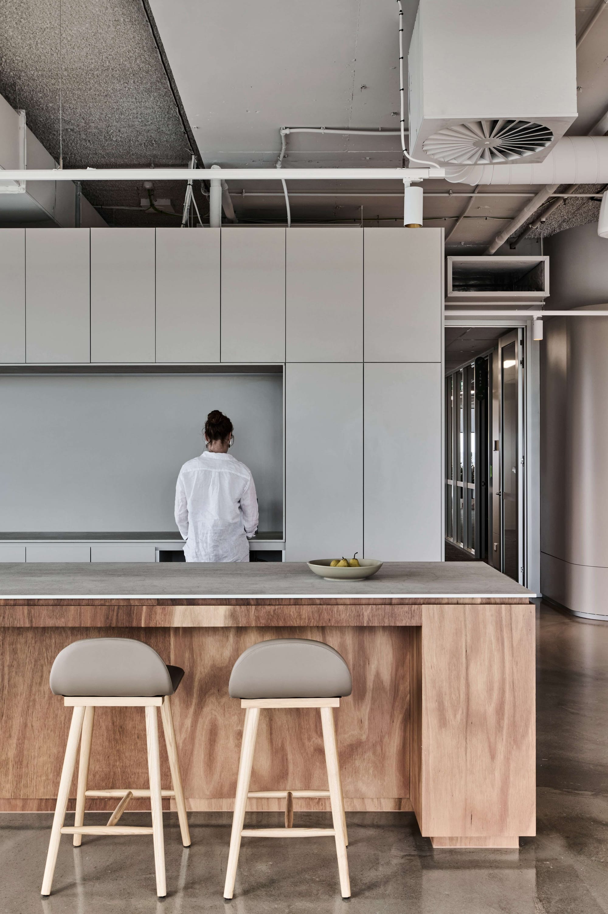 Icon HQ by FIGR. Office kitchen featuring varnished plywood kitchen island and light grey fitted cabinets.