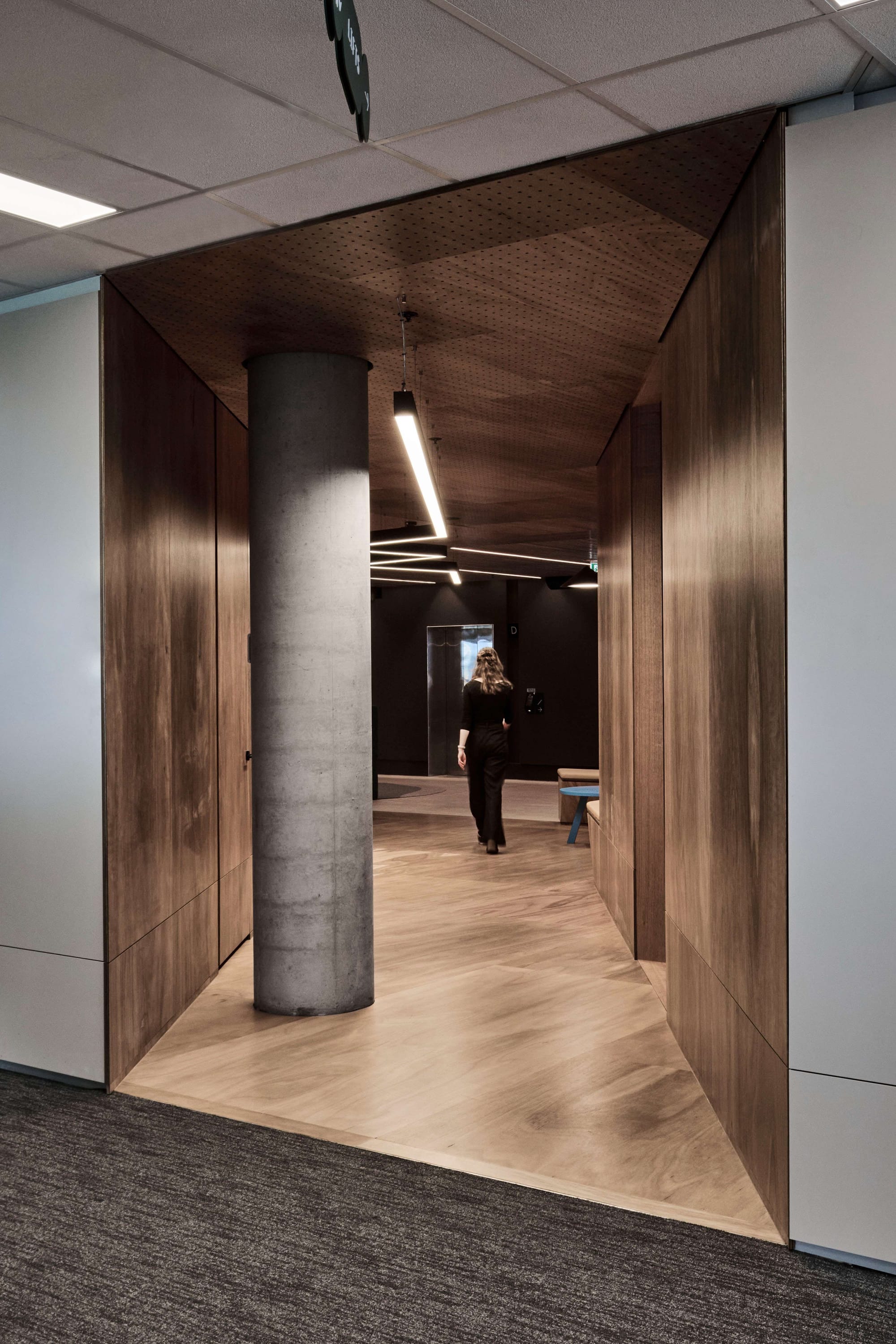 Icon HQ by FIGR. Wood covered corridor featuring perforated ceiling and concrete pillar.