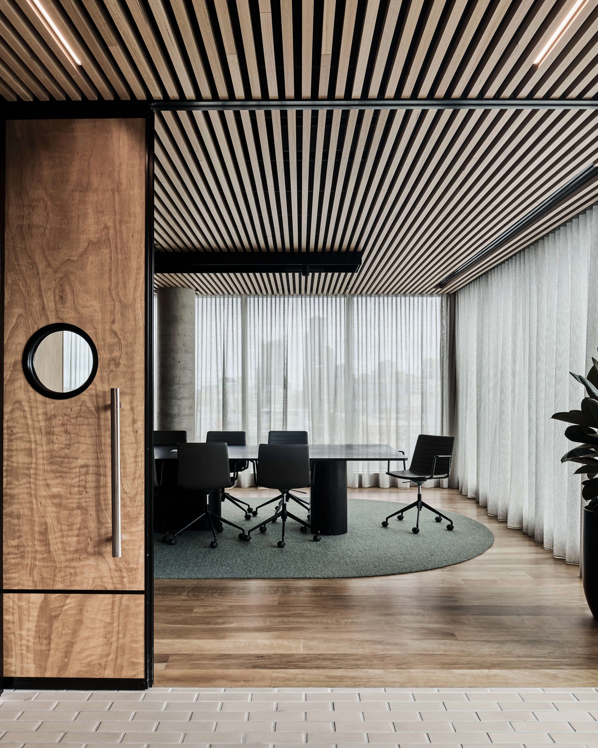 Icon HQ by FIGR. Office conference room entrance featuring customised, wooden sliding door with view on black table, vitra chairs.