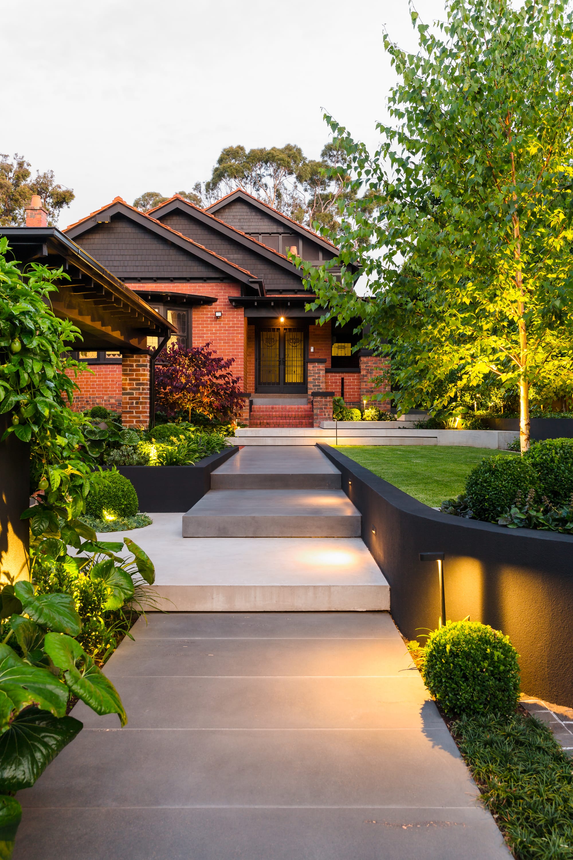 Outside view on red brick house featuring garden and layered concrete hardscaping stairway. 