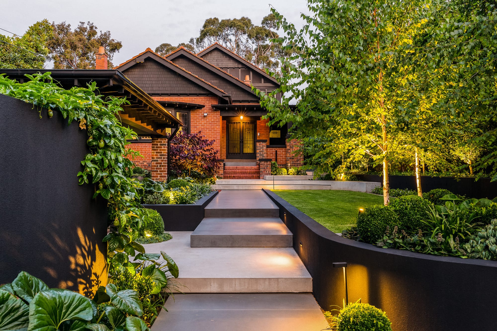 Outside view on red brick house featuring garden and layered concrete hardscaping stairway. 