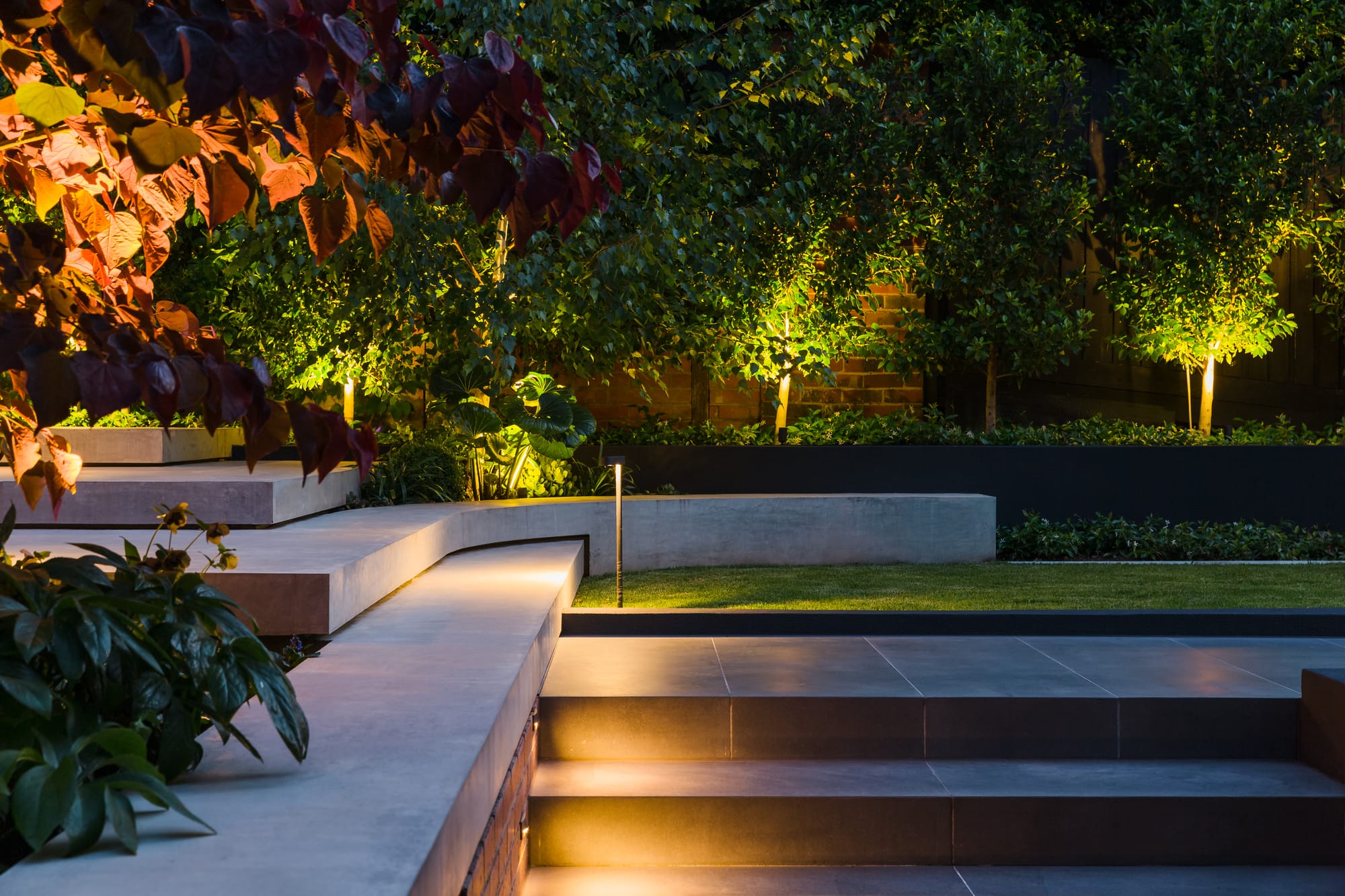 View on garden at night with illumination featuring layered concrete hardscaping and staircase.