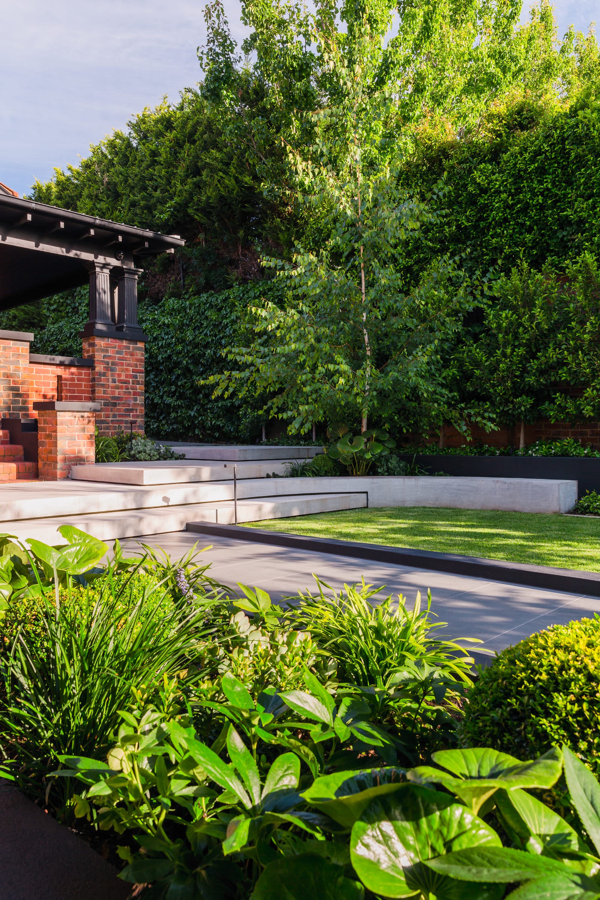 Garden featuring layered concrete hardscaping and stone staircase and red brick house.