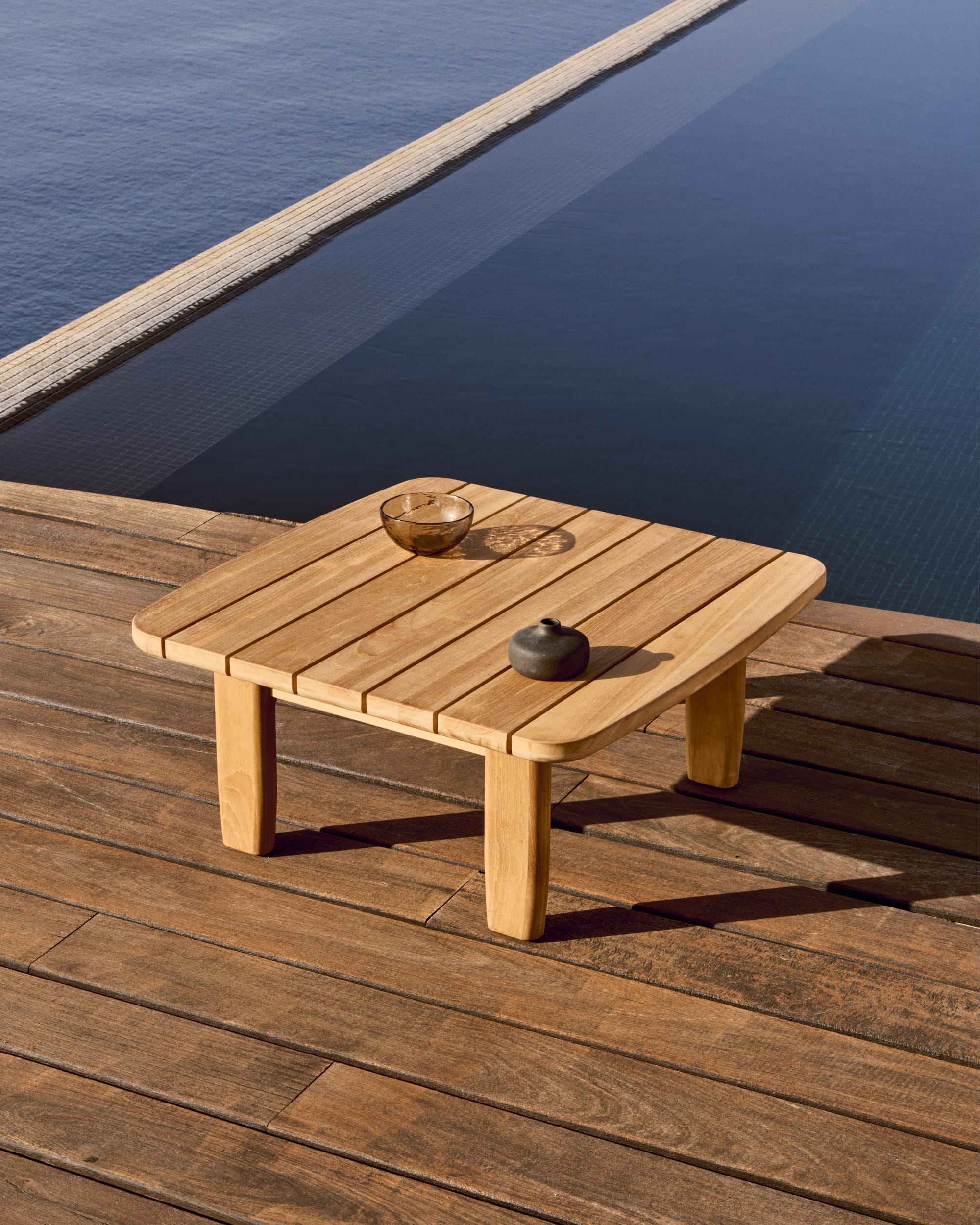 Tirant by Kave Home. Teak wood outdoor coffee table on terrace with pool and ocean view.