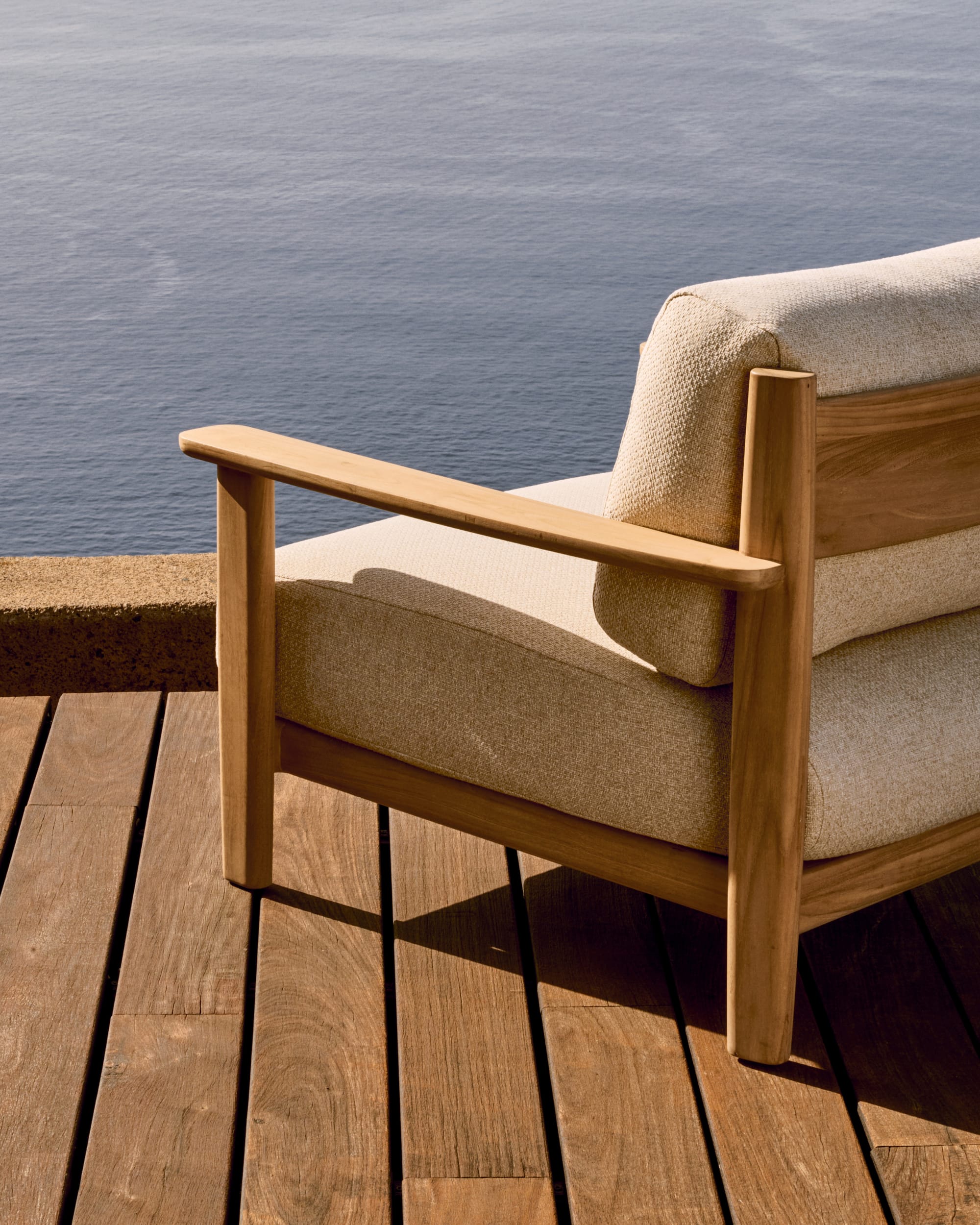 Tirant by Kave Home. Teak wood outdoor sofa featuring beige accent fabric on terrace with ocean view.