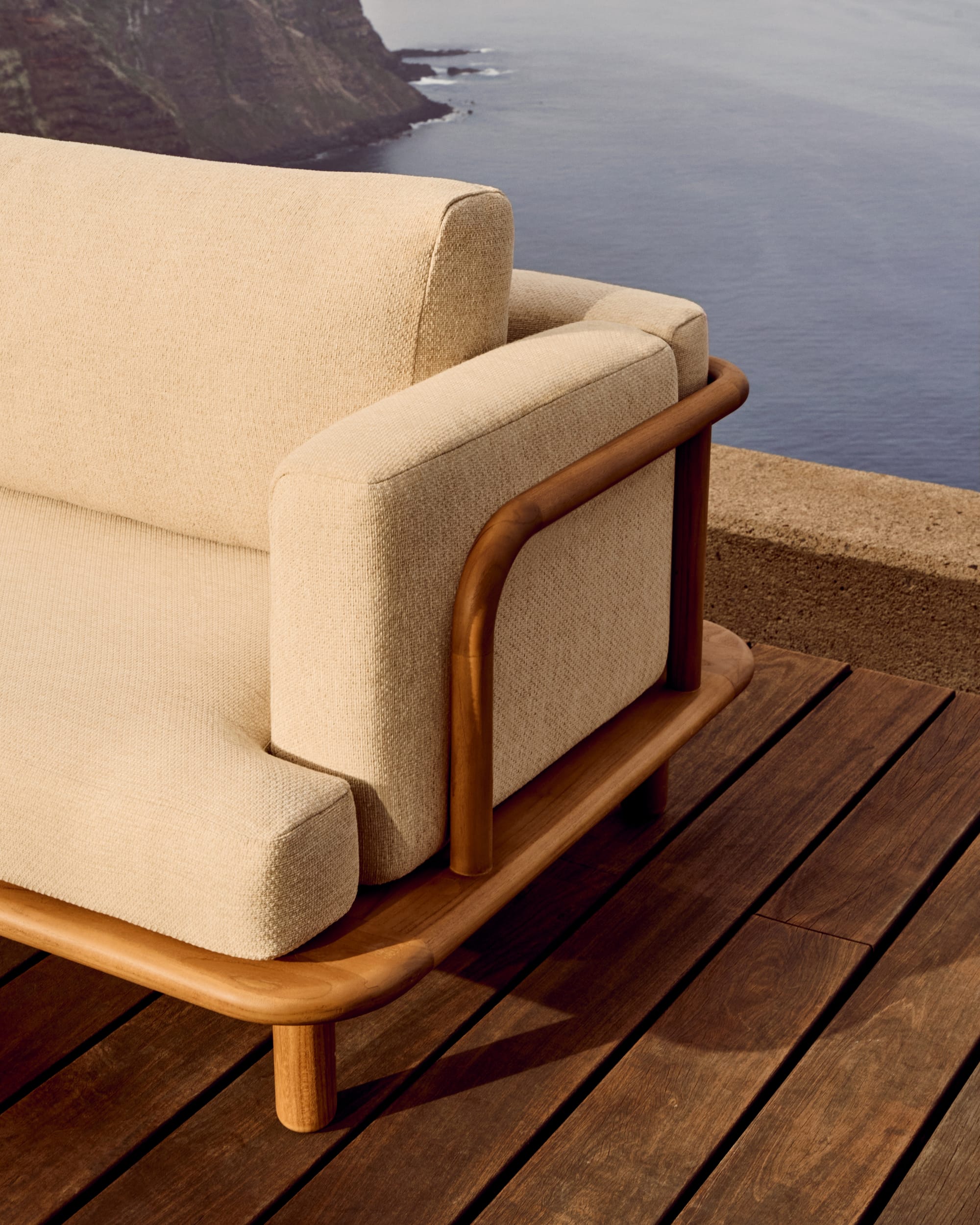 Turquetta by Kave Home. Curved teak wood outdoor sofa featuring beige accent fabric and ocean view.