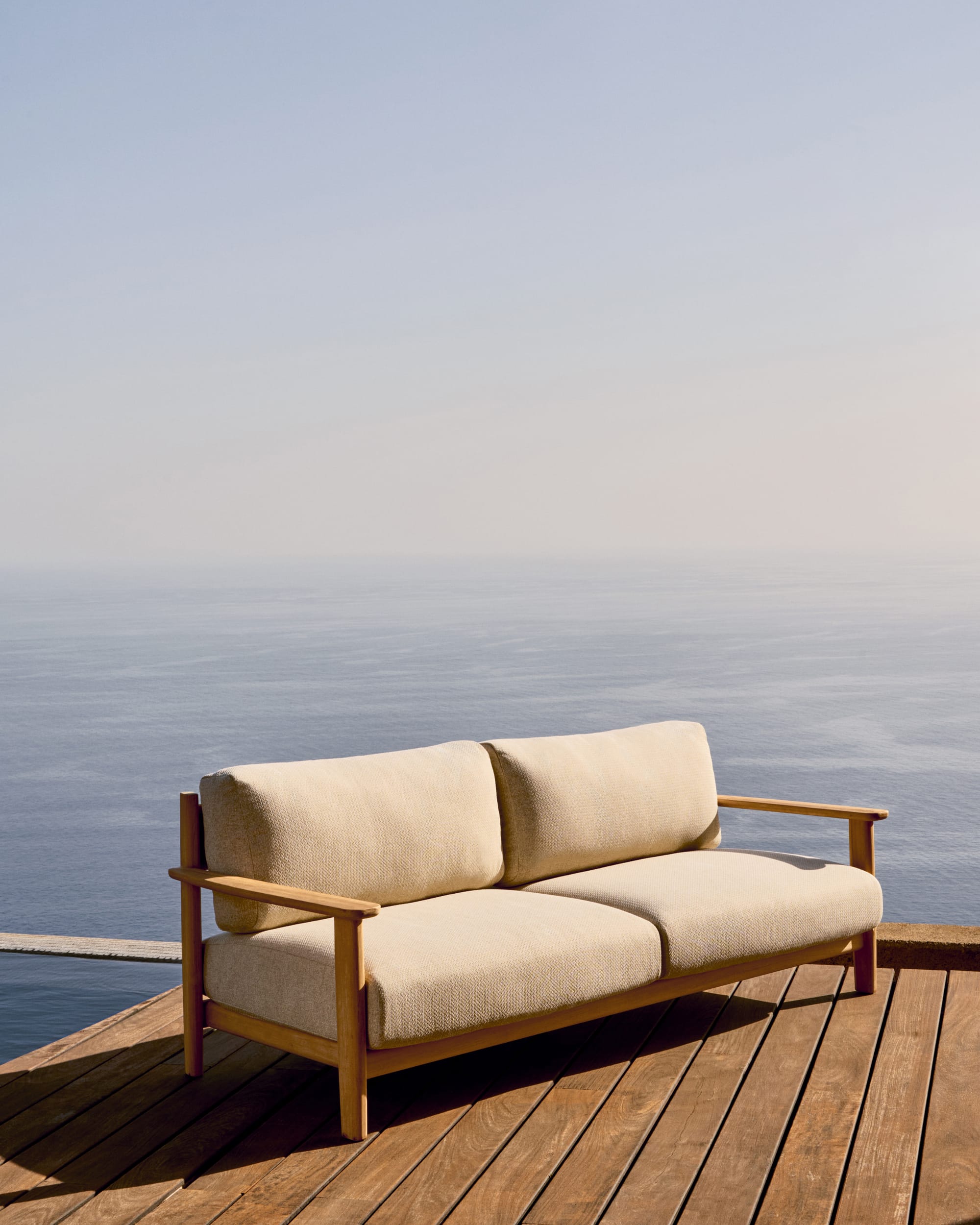 Tirant by Kave Home. Teak wood outdoor sofa featuring beige accent fabric on terrace with ocean view.